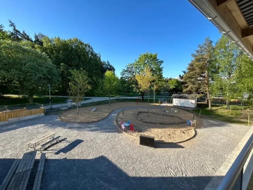 Utsikt över gården med sandlåda, planteringar och picknickbänkar