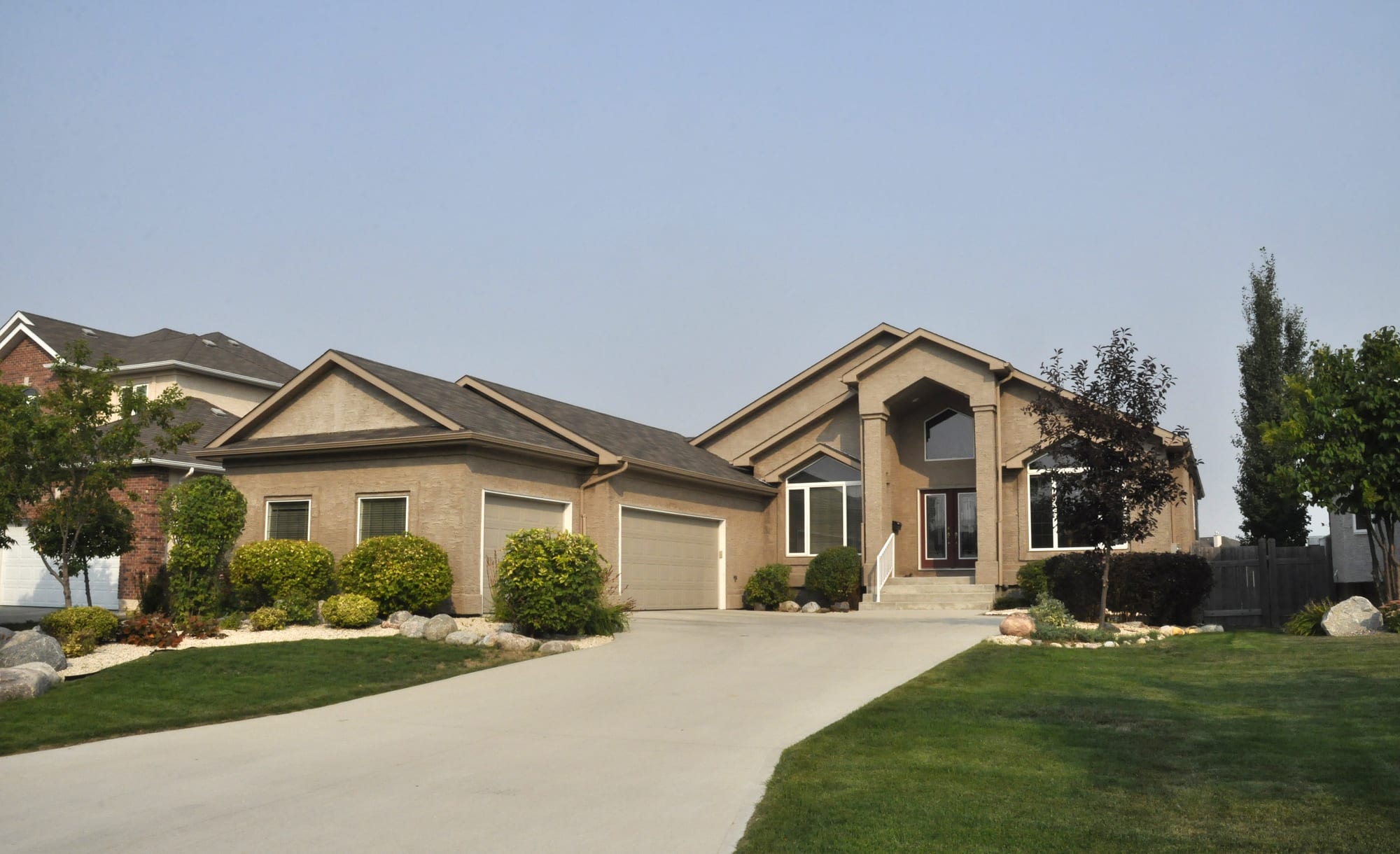Tan stucco single-family home seen from the street, a wide poured concrete driveway sweeping up to its three-car garage