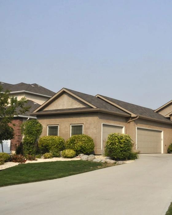 Tan stucco single-family home seen from the street, a wide poured concrete driveway sweeping up to its three-car garage