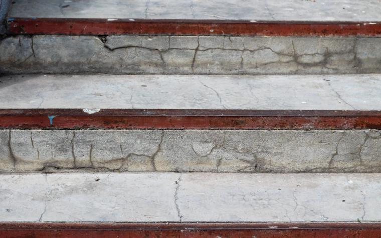 Close-up of exterior concrete steps whose treads and risers are broken by a network of cracks, with rusting painted metal nosing strips along each tread