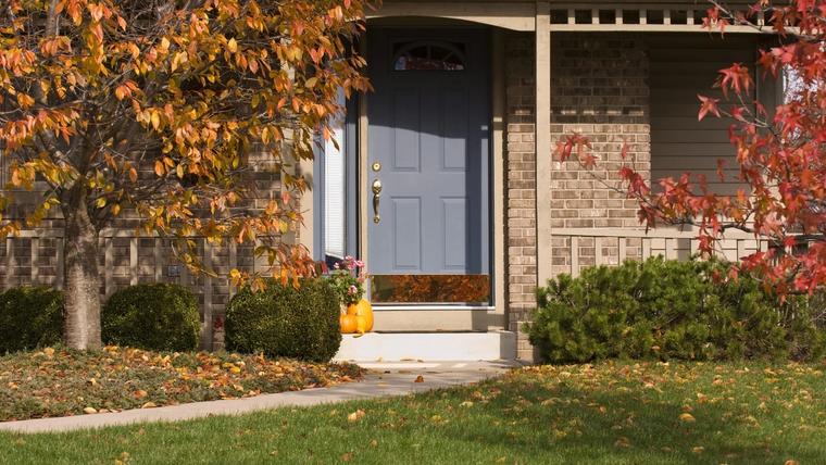 Poured concrete stoop and front walk at the door of a brick-and-siding suburban house, autumn leaves on the lawn and a maple turning orange beside it