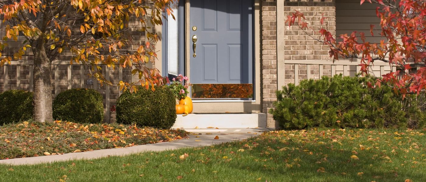 Poured concrete stoop and front walk at the door of a brick-and-siding suburban house, autumn leaves on the lawn and a maple turning orange beside it