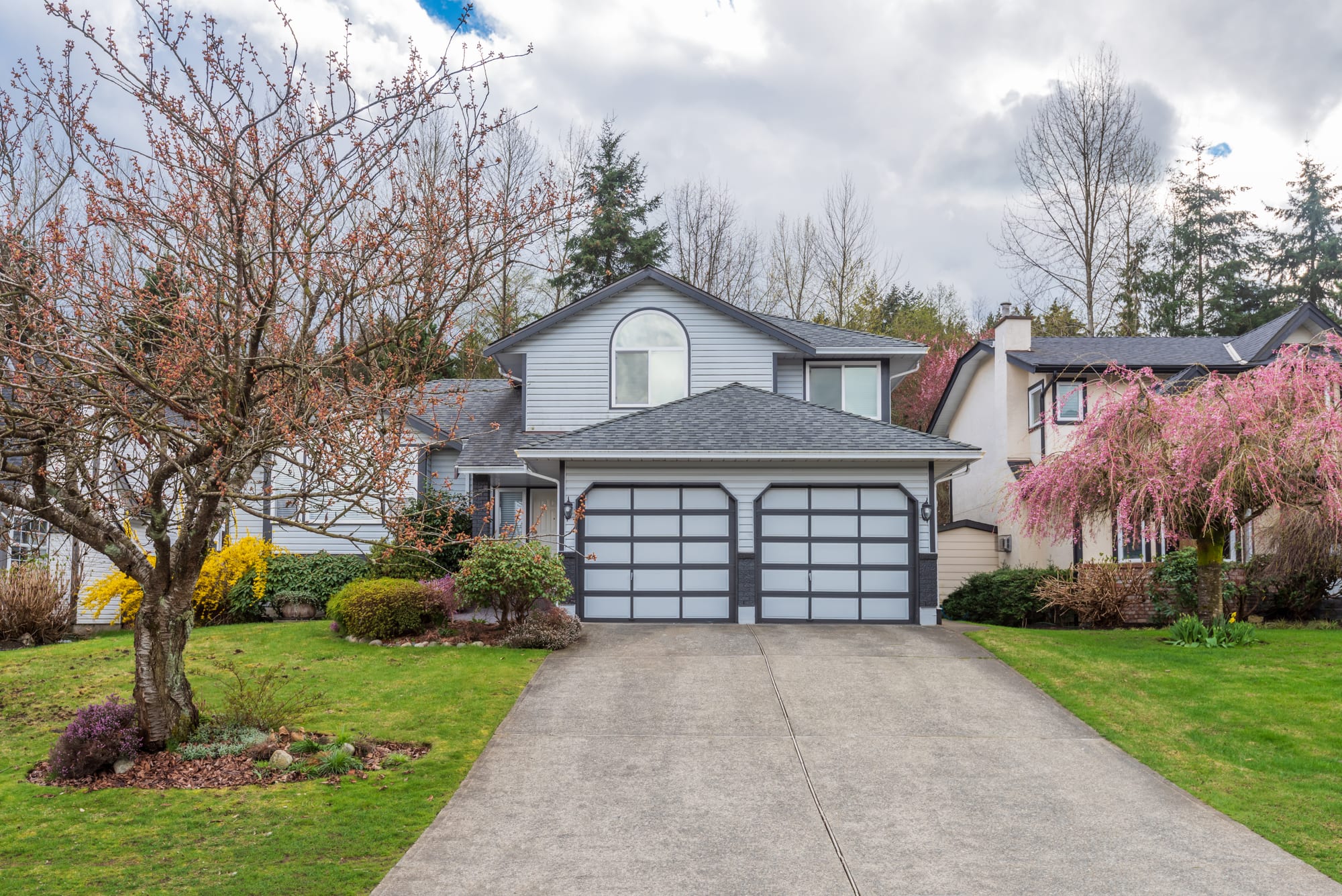 Wide poured concrete driveway with an open control joint running up to the two-car garage of a suburban home on an overcast spring day