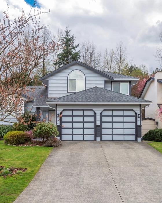 Wide poured concrete driveway with an open control joint running up to the two-car garage of a suburban home on an overcast spring day