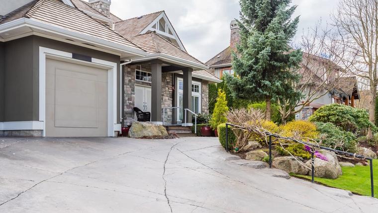 Concrete driveway in front of a suburban home with a long crack and an open control joint running across the slab