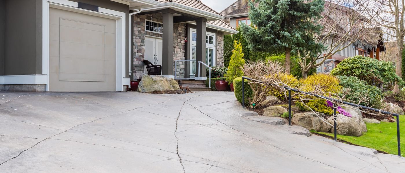 Concrete driveway in front of a suburban home with a long crack and an open control joint running across the slab