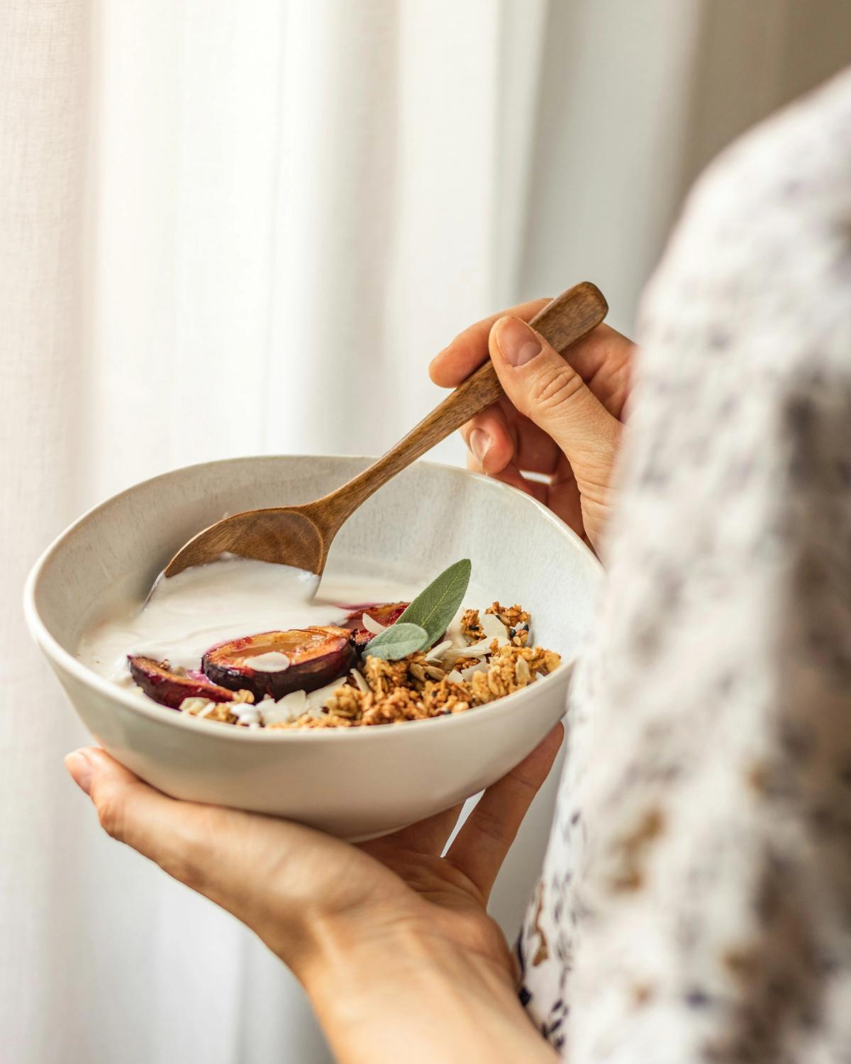 Hands holding a breakfast bowl of porridge topped with plums