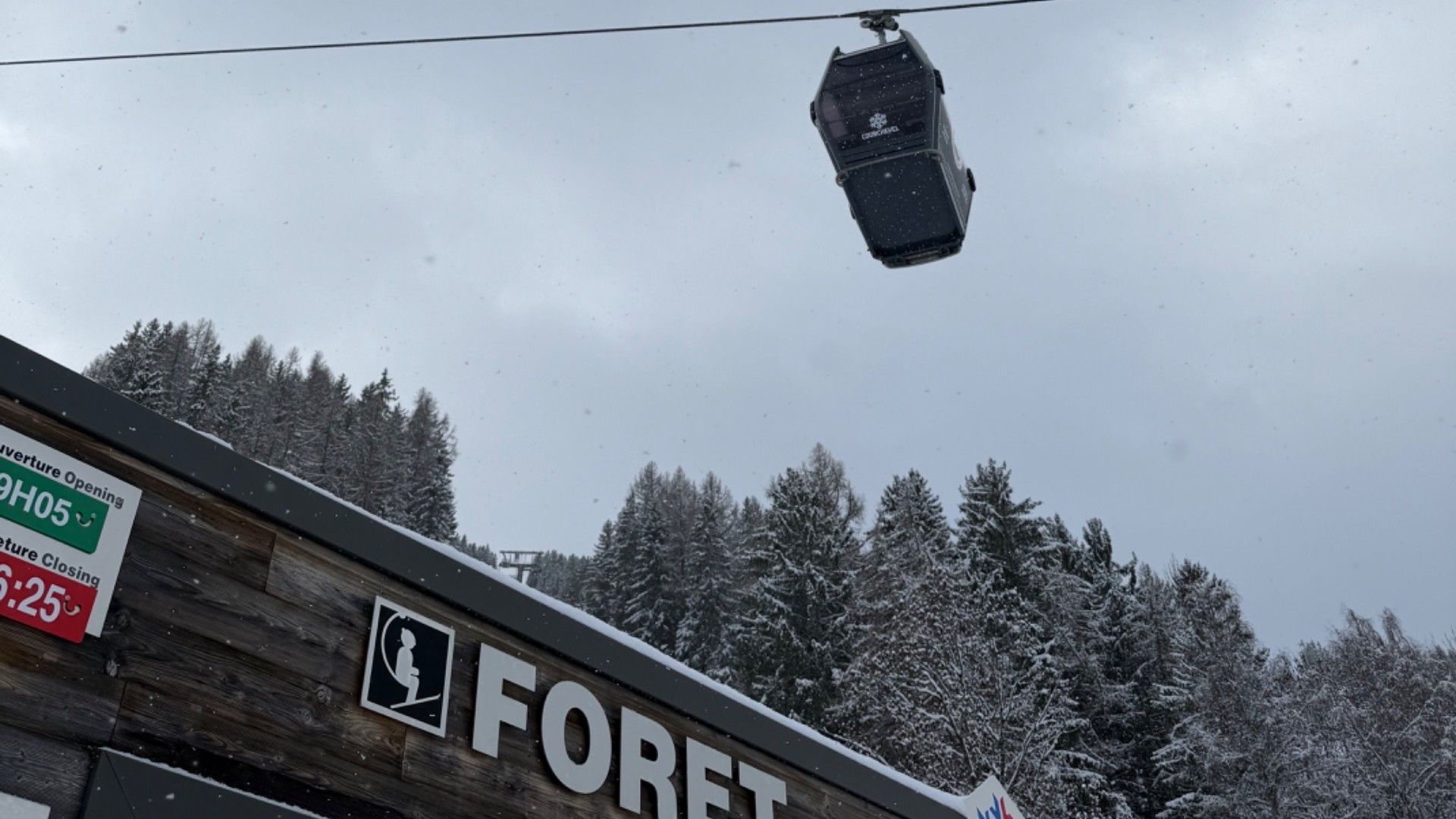 The Forêt lift station in snowy Le Praz, with a lift cabin overhead and snow-covered trees behind.