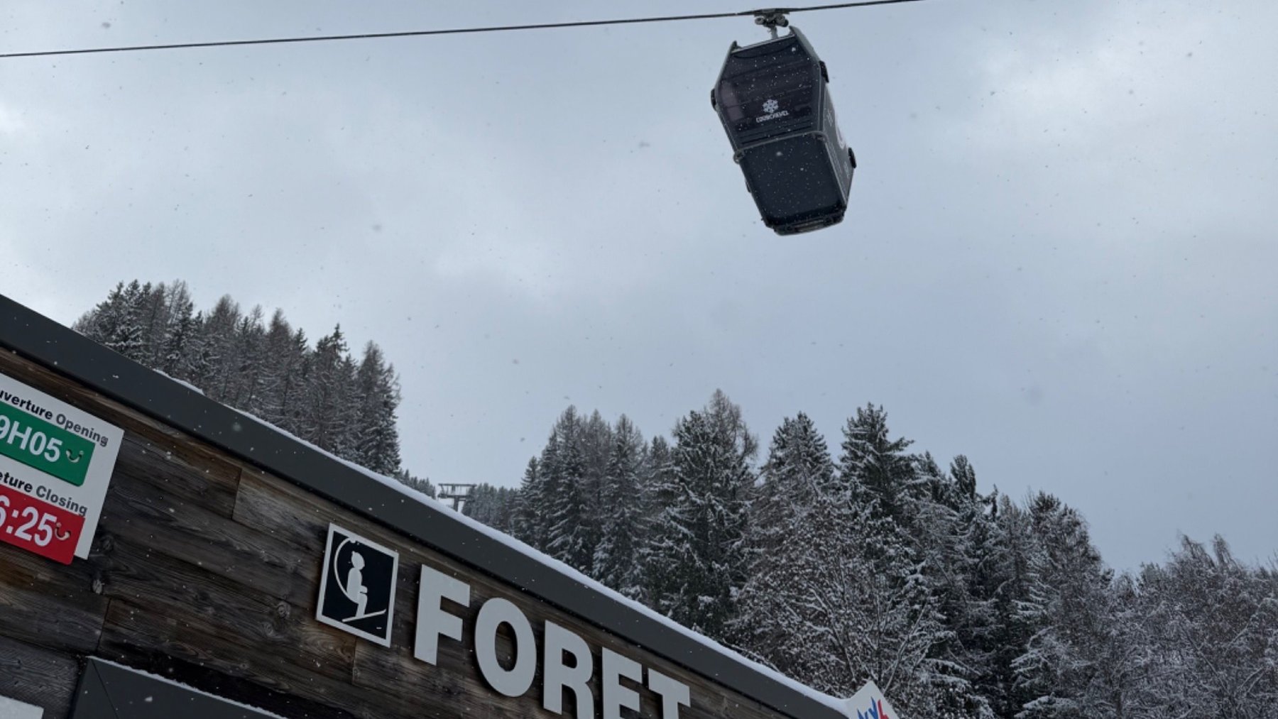 The Forêt lift station in snowy Le Praz, with a lift cabin overhead and snow-covered trees behind.