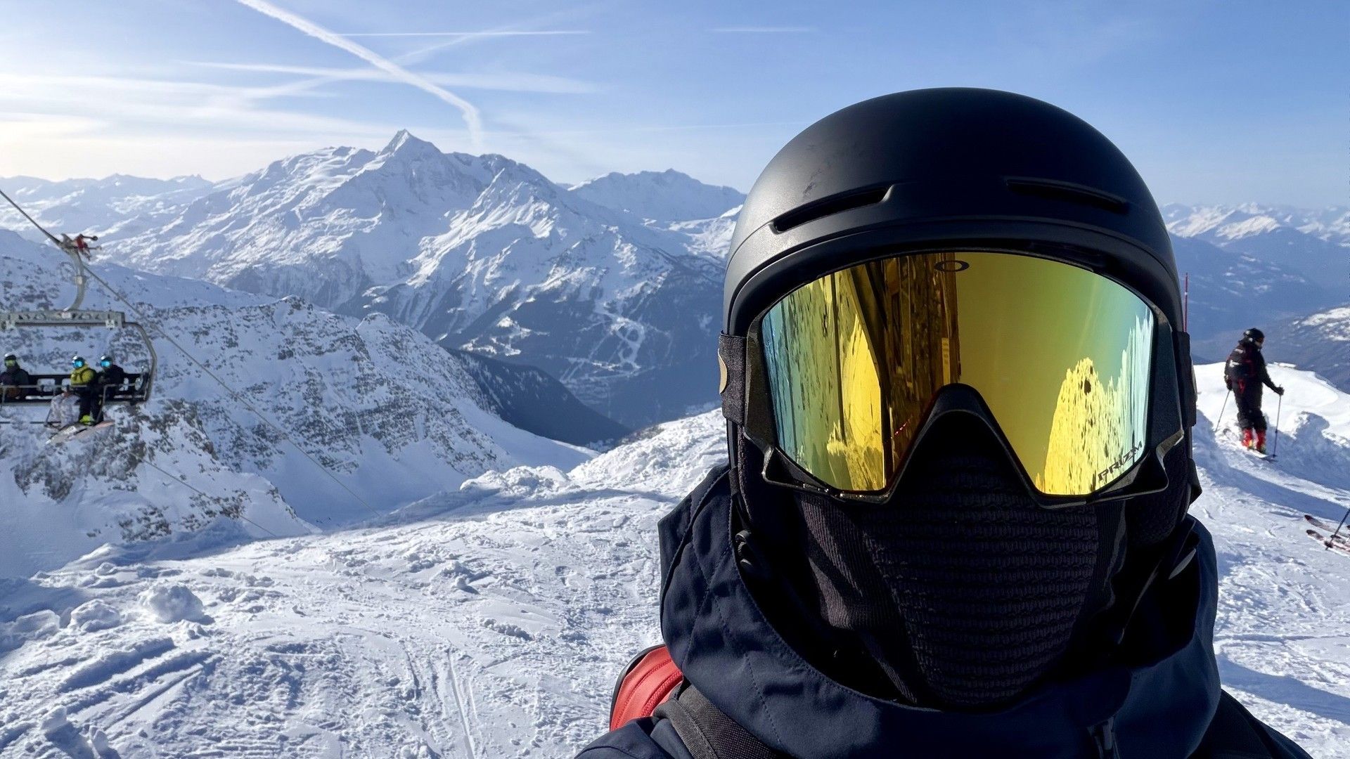 Skier in a helmet and mirrored goggles poses on a snowy slope with La Rosière's mountains behind