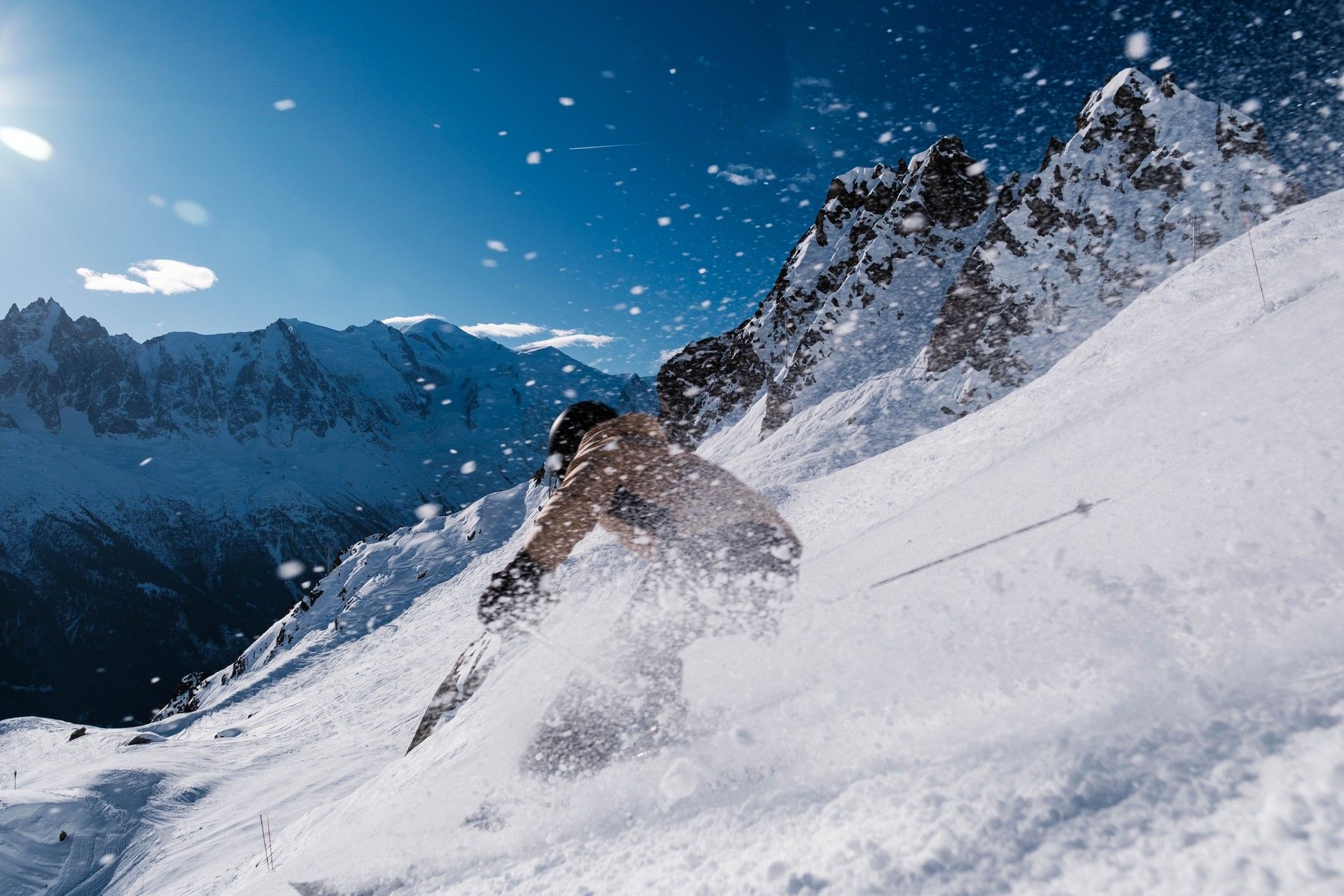 Skiers carve across snowy alpine slope as powder sprays from a dramatic rightward jump.