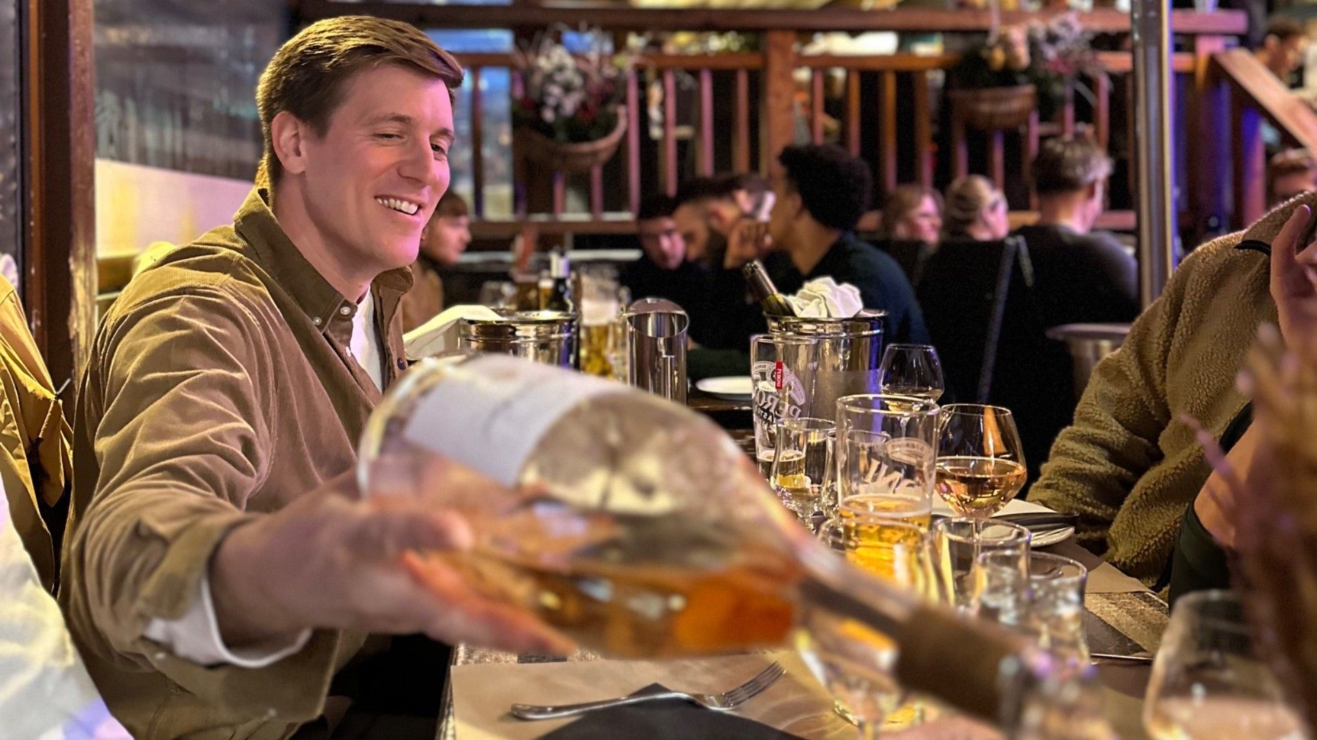 Friends share drinks at a restaurant during a group ski trip as a man pours wine at the table.
