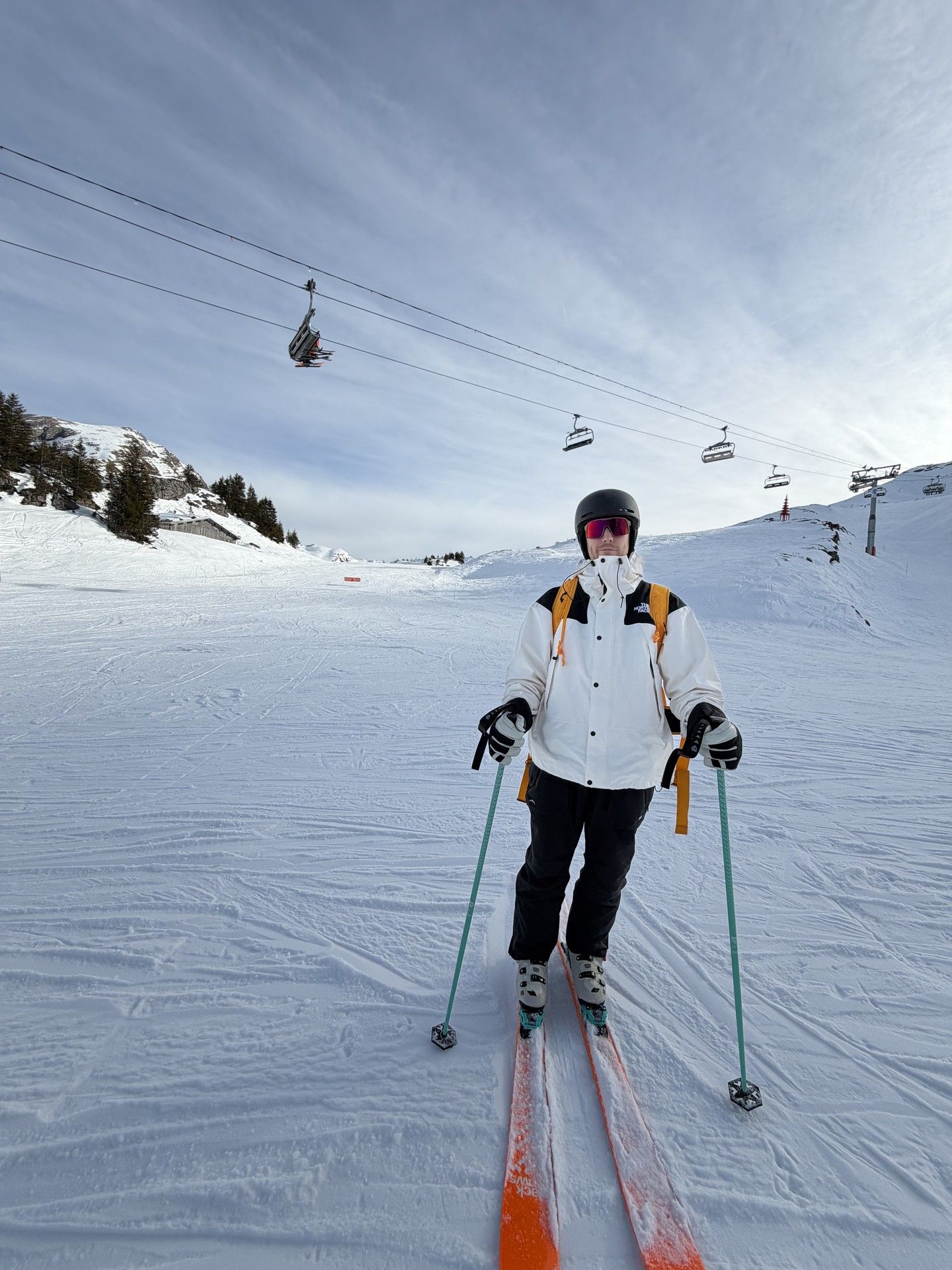 Skiing instructor in ski gear with poles on a snowy slope near chairlifts and a cableway
