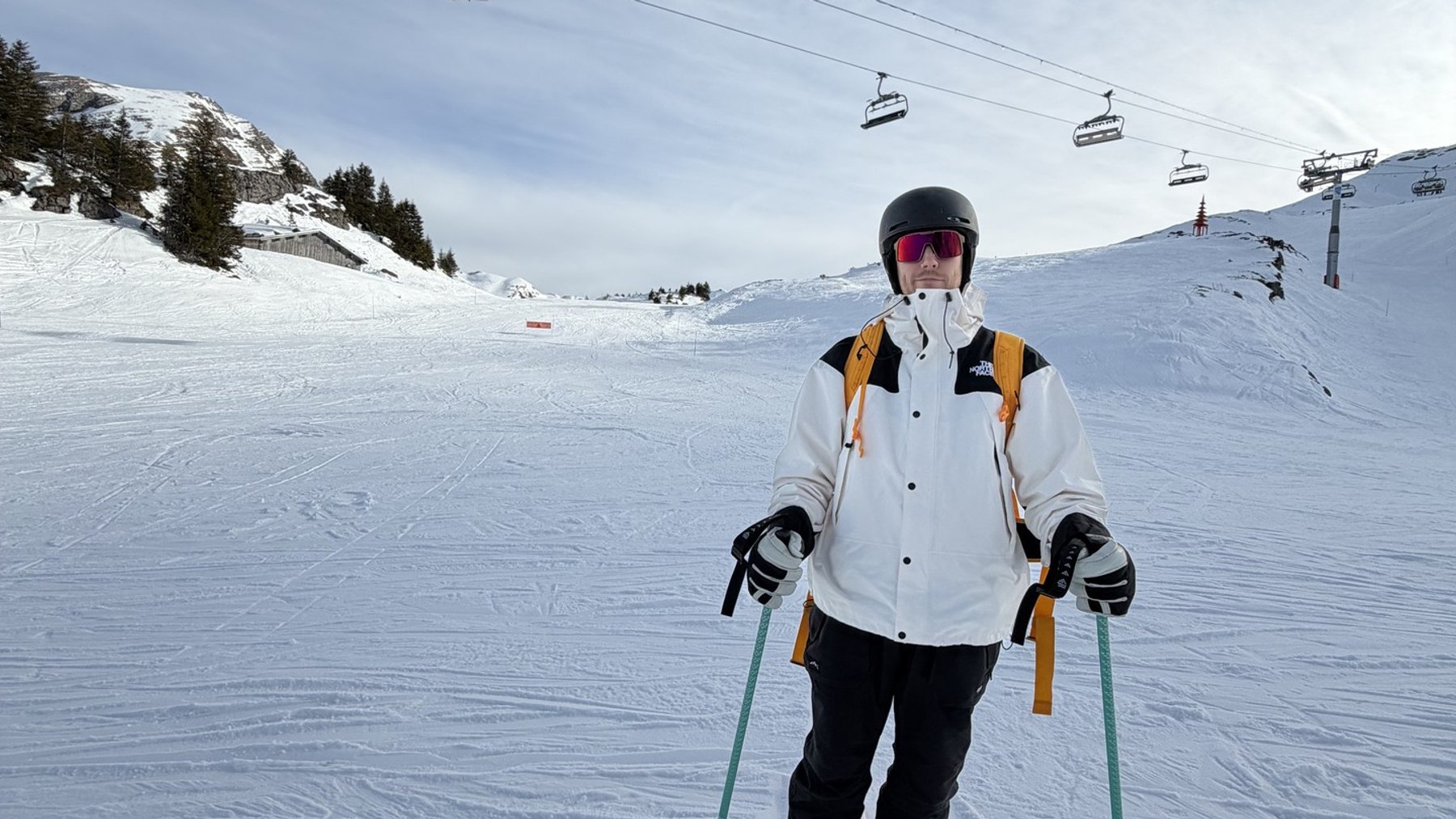 Skiing instructor in ski gear with poles on a snowy slope near chairlifts and a cableway