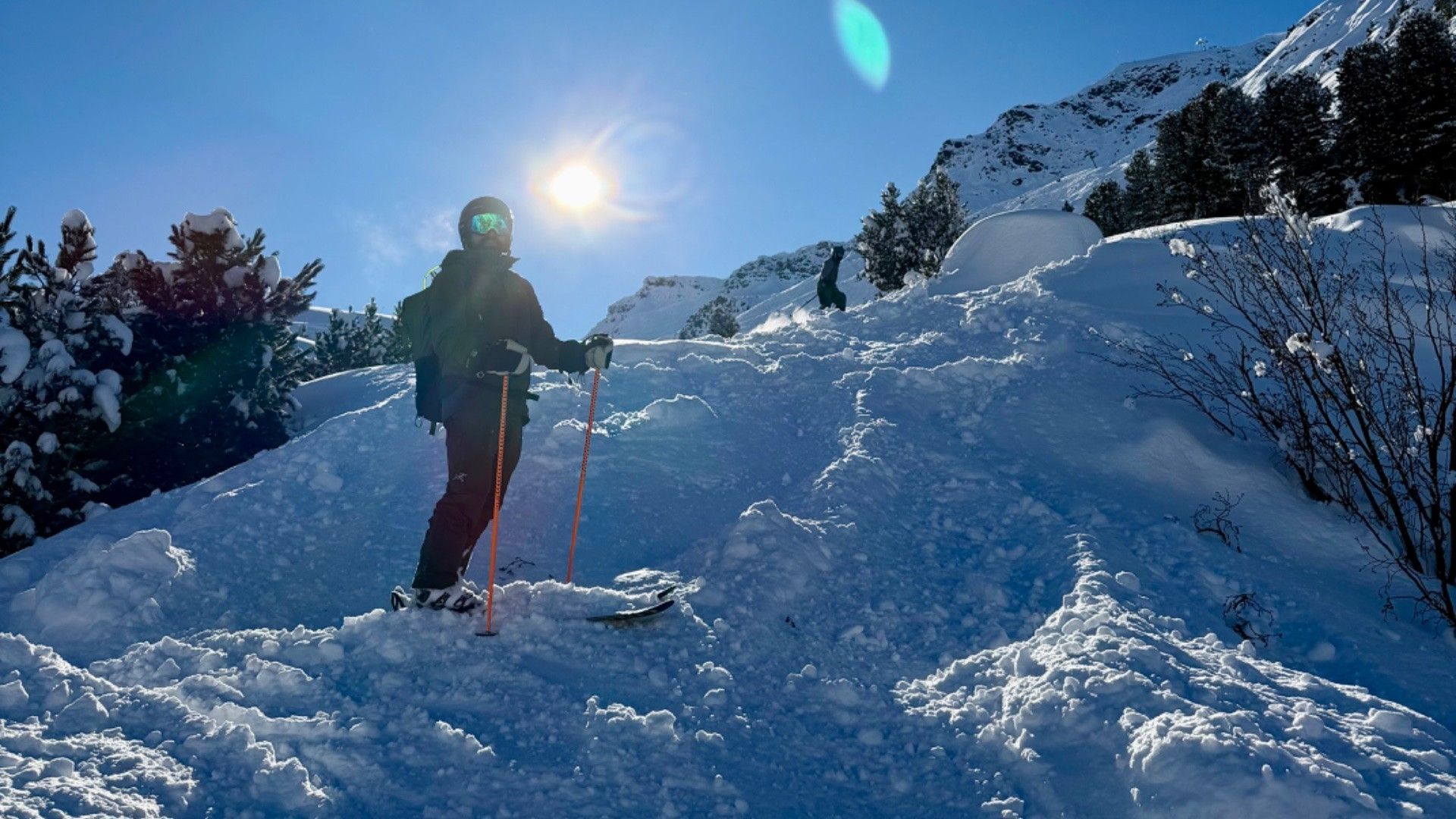 Skier climbs a snowy slope in Courchevel, with the sun behind them and a mountain ridge in the background.
