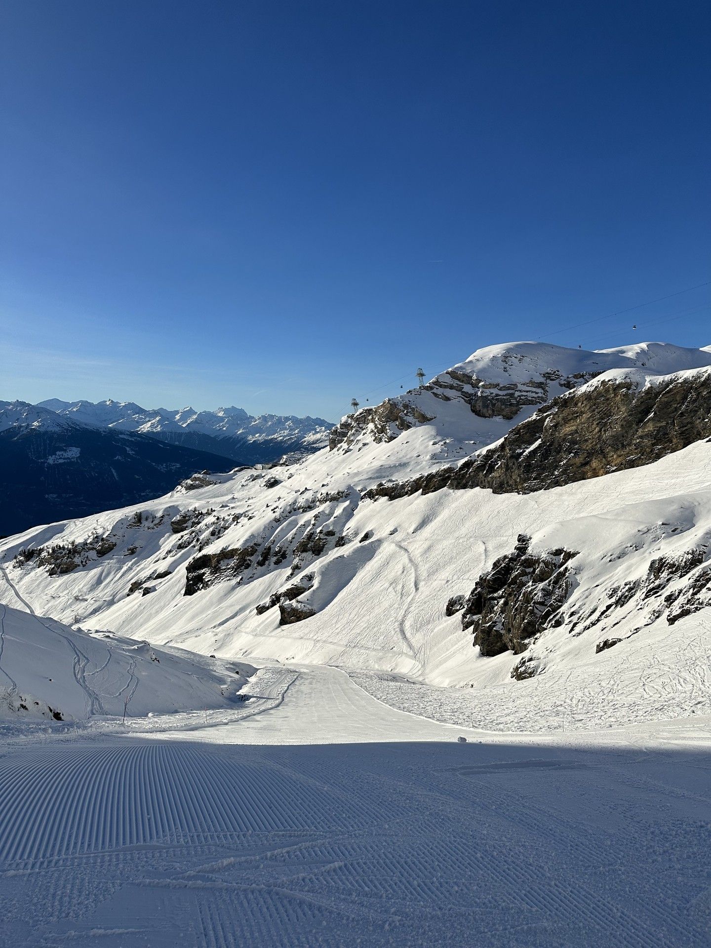 Snow-covered alpine slopes under clear blue sky with distant mountain ridgelines