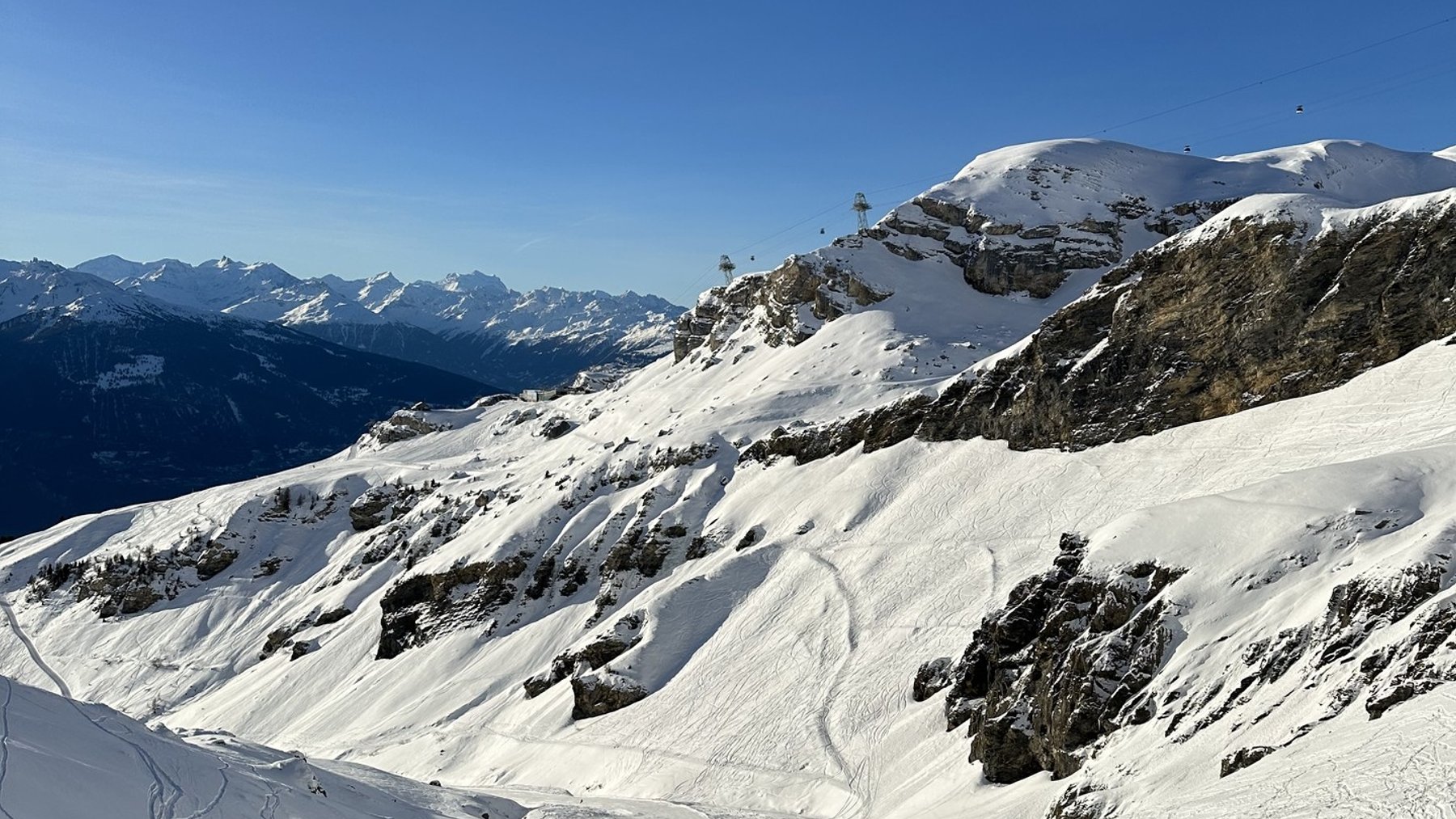 Snow-covered alpine slopes under clear blue sky with distant mountain ridgelines