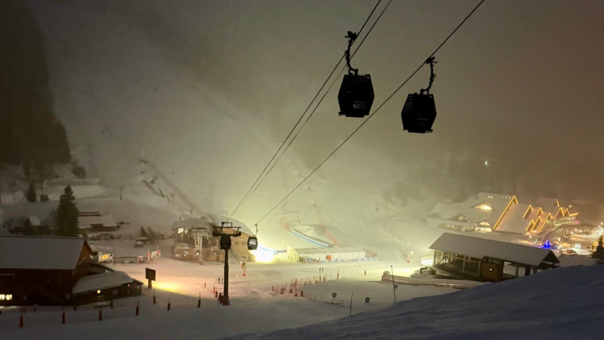 Snowy ski slope at night beneath gondola cabins, with the lights of Méribel glowing below
