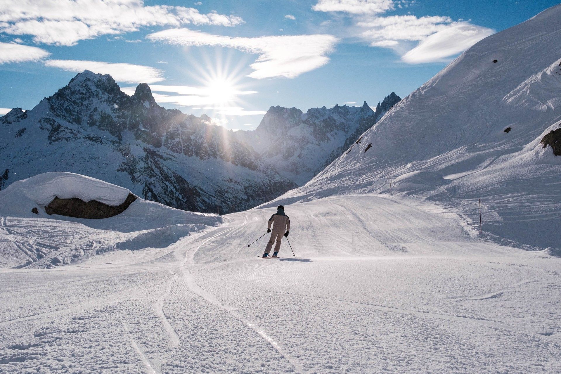 Skiers on a snowy alpine slope with mountain peaks and bright sunrise in the background
