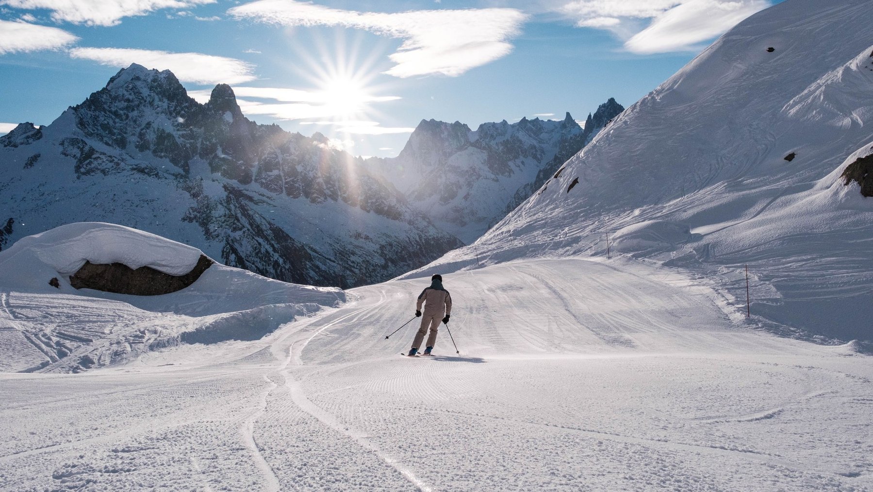 Skiers on a snowy alpine slope with mountain peaks and bright sunrise in the background