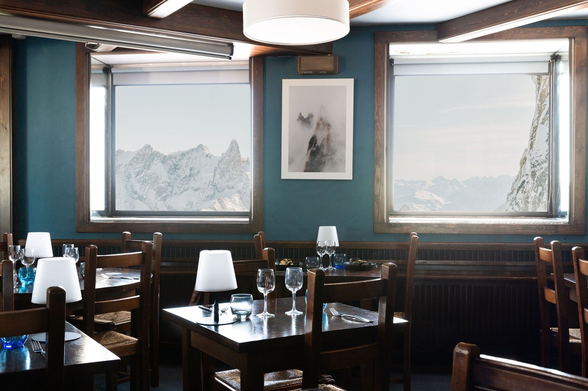 Cozy mountain-view restaurant dining tables with glasses and blue bottles by large windows
