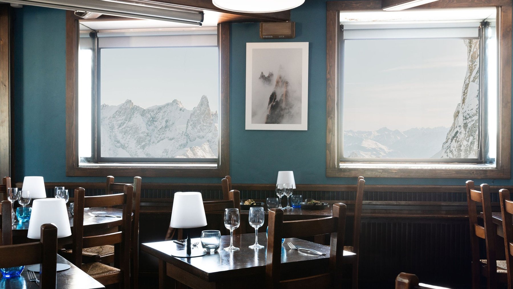 Cozy mountain-view restaurant dining tables with glasses and blue bottles by large windows