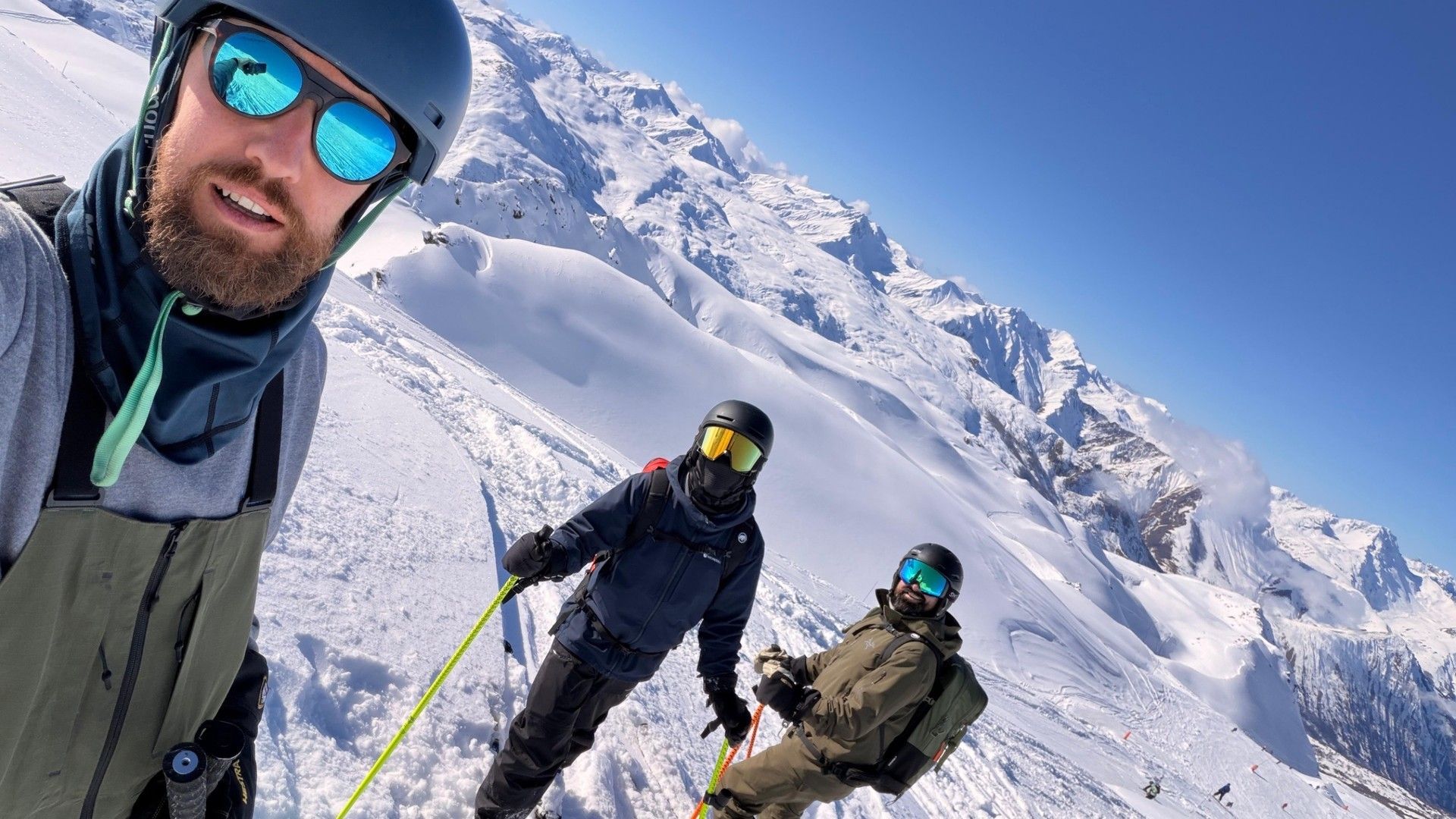 Three skiers on a steep snowy slope in Courchevel, with rugged Alpine peaks behind them.