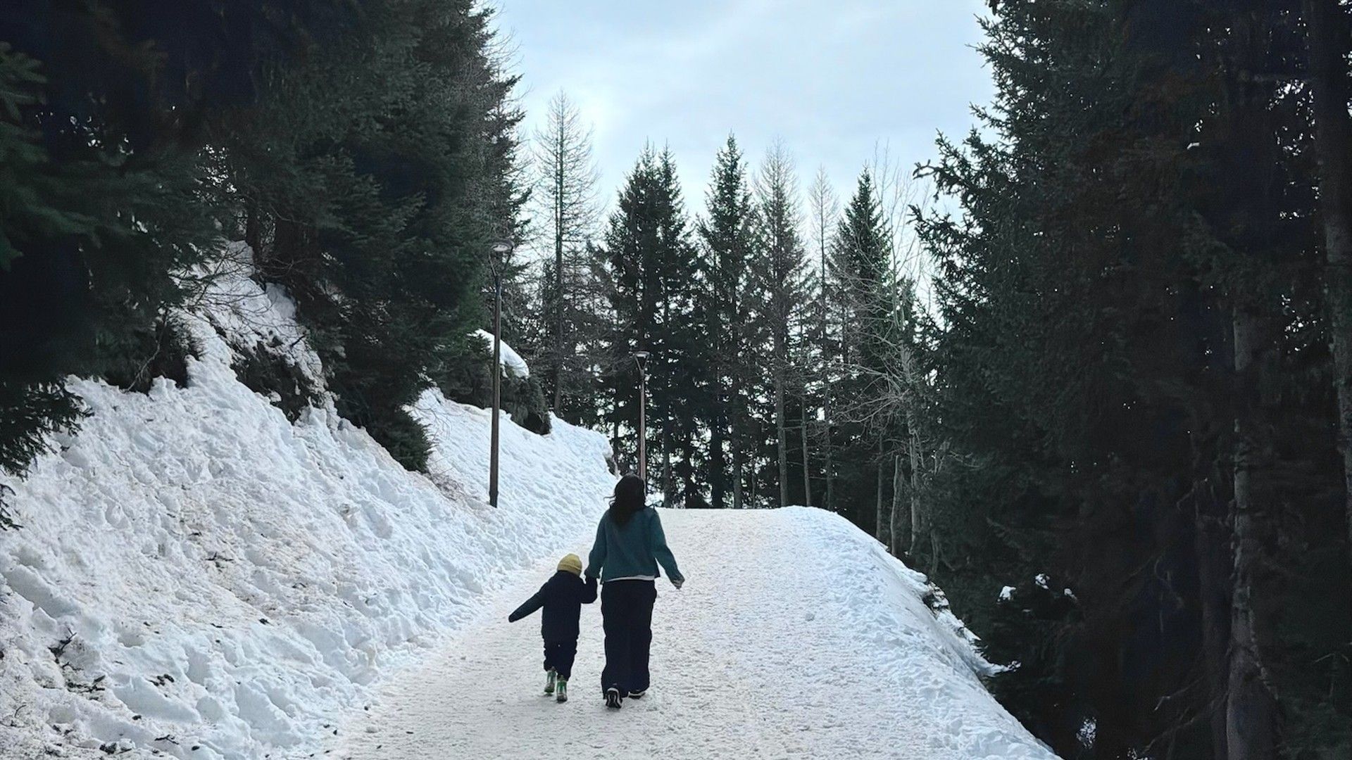 Two people walk uphill along a snowy forest trail in La Rosière.