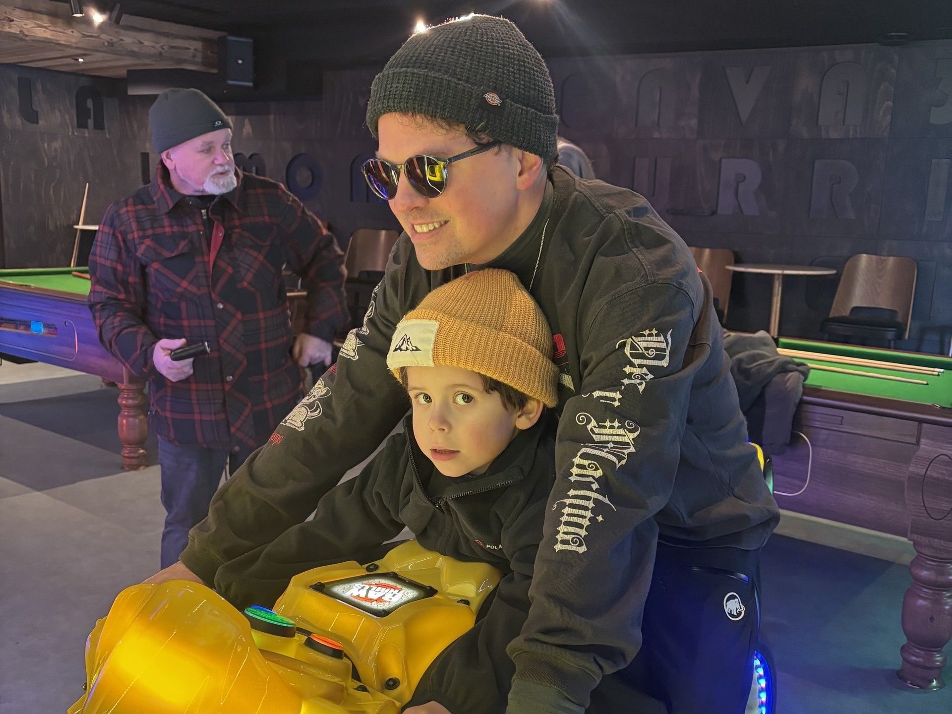 Family skiing session indoors, father holding child beside rental skis and gear under warm lights