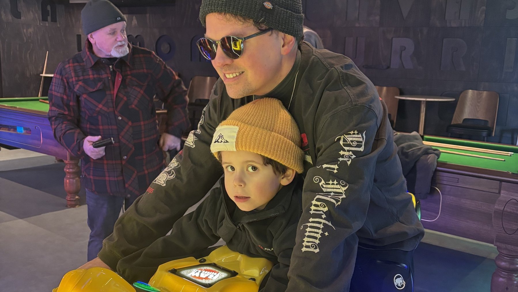 Family skiing session indoors, father holding child beside rental skis and gear under warm lights
