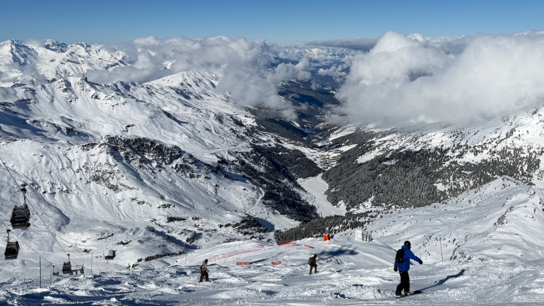 Skiers descend a snowy Courchevel piste, with the Alps and clouds stretching across the horizon.