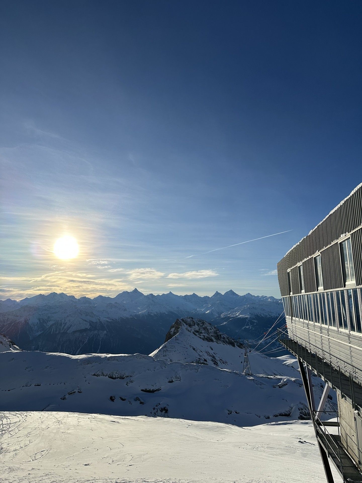Snowy mountain sunrise with a ski lodge balcony overlooking the peaks and pistes