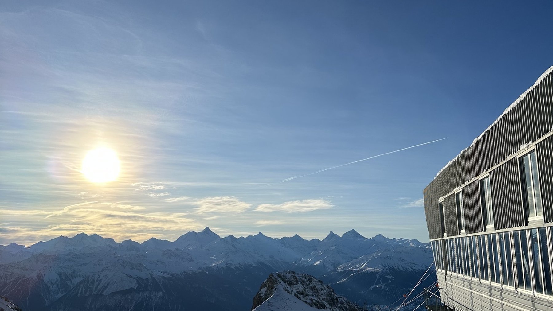 Snowy mountain sunrise with a ski lodge balcony overlooking the peaks and pistes