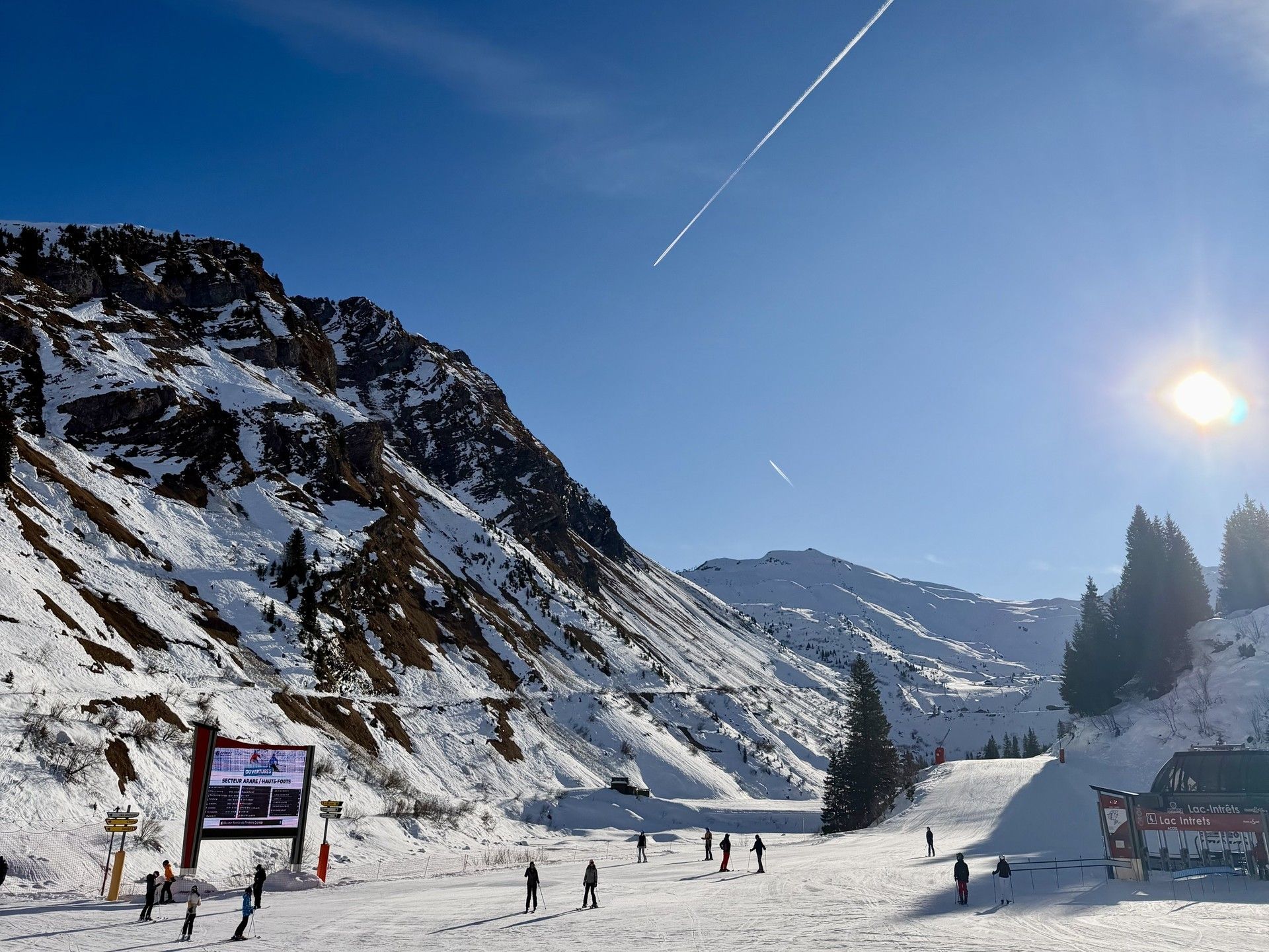 Skiers on a snowy alpine slope under clear blue sky with bright sun and falling light streaks