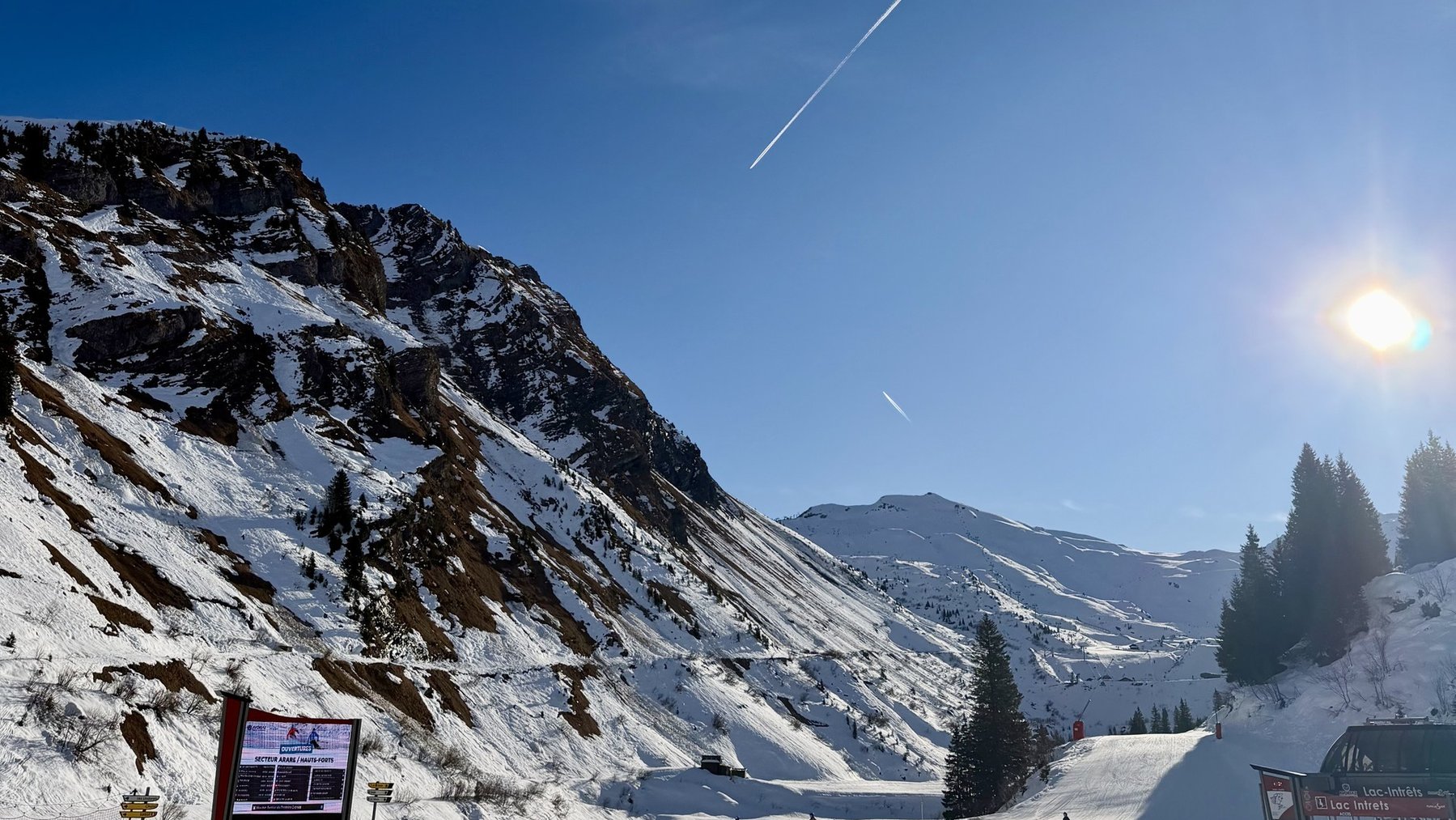 Skiers on a snowy alpine slope under clear blue sky with bright sun and falling light streaks