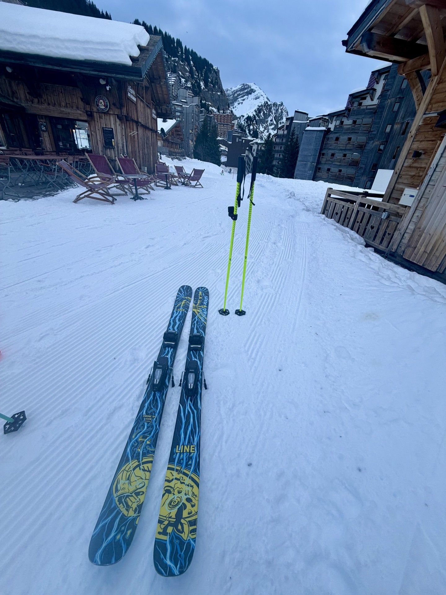 Skis and poles laid on snowy ground outside a mountain chalet, ready for a ski day.