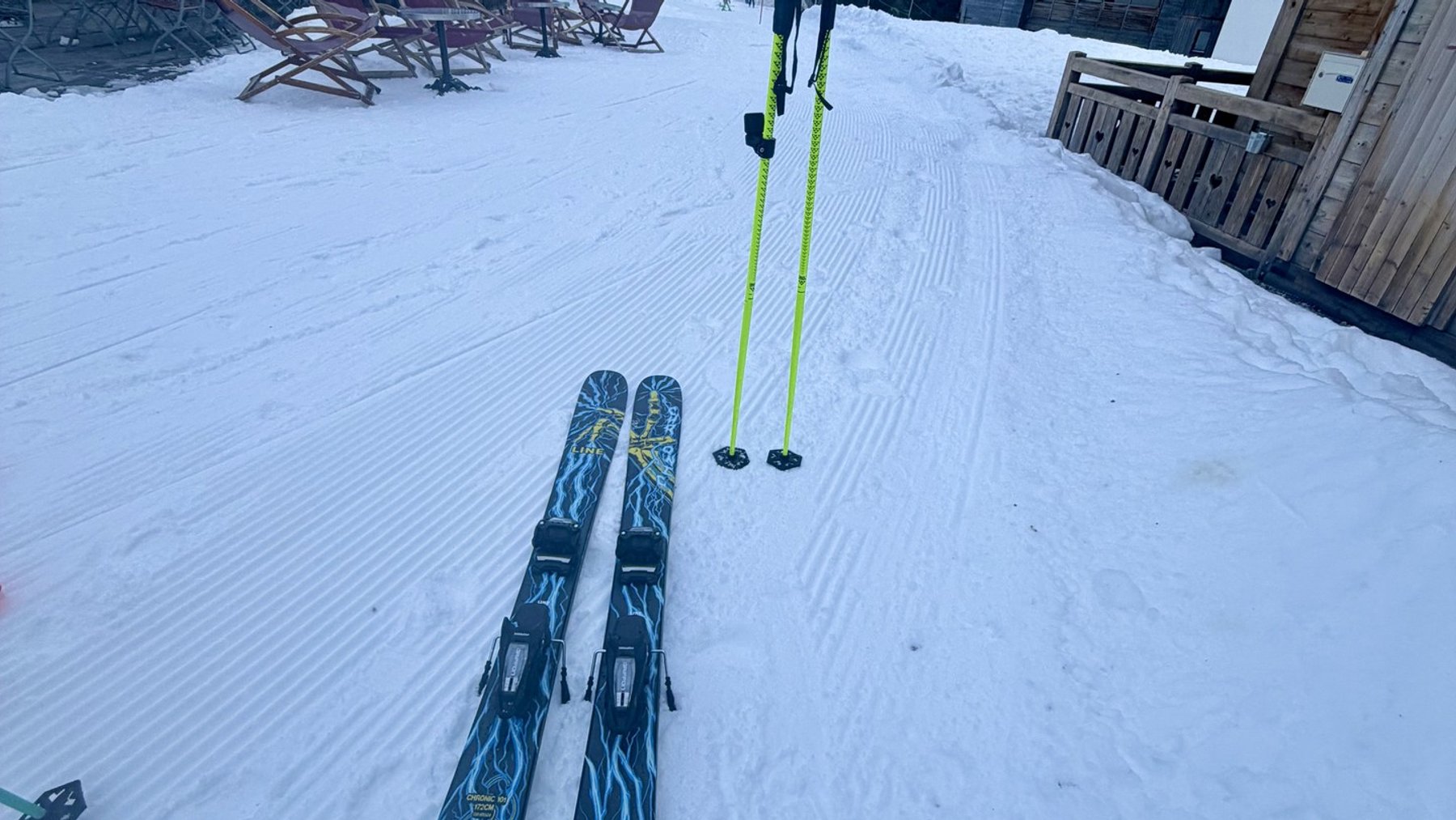 Skis and poles laid on snowy ground outside a mountain chalet, ready for a ski day.