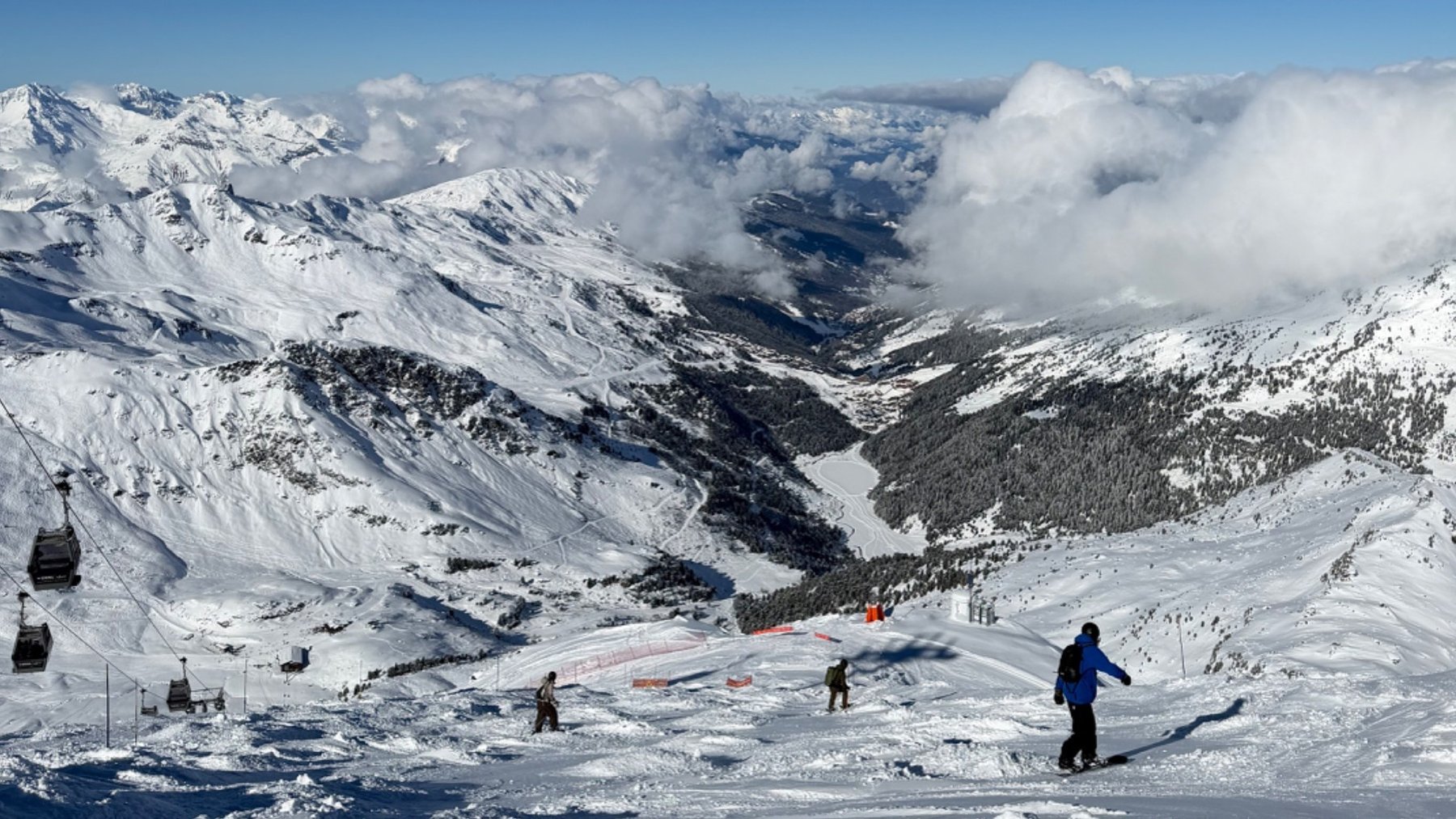 Skiers descend a snowy Courchevel piste with the Alps and clouds stretching across the background.