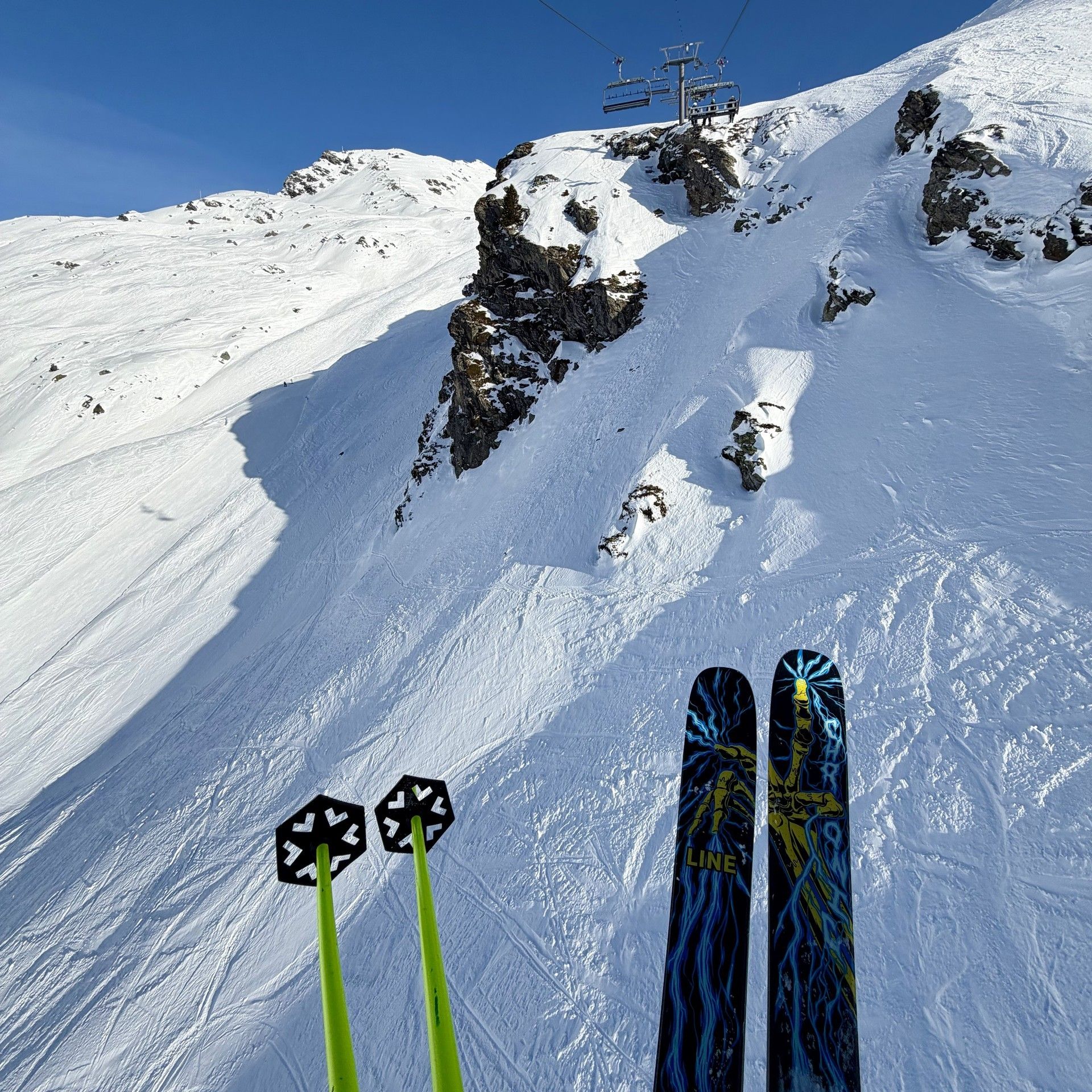 Skier’s skis and poles point uphill toward a lift on a steep, snowy slope at La Rosière