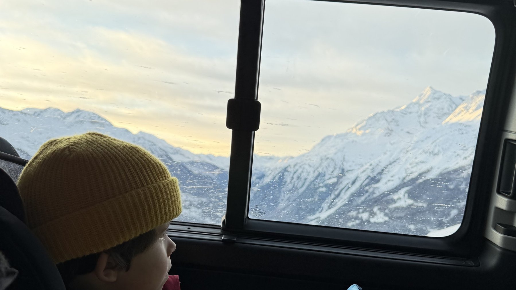 Child in a ski trip car seat playing with a tablet while mountains snow peaks outside window