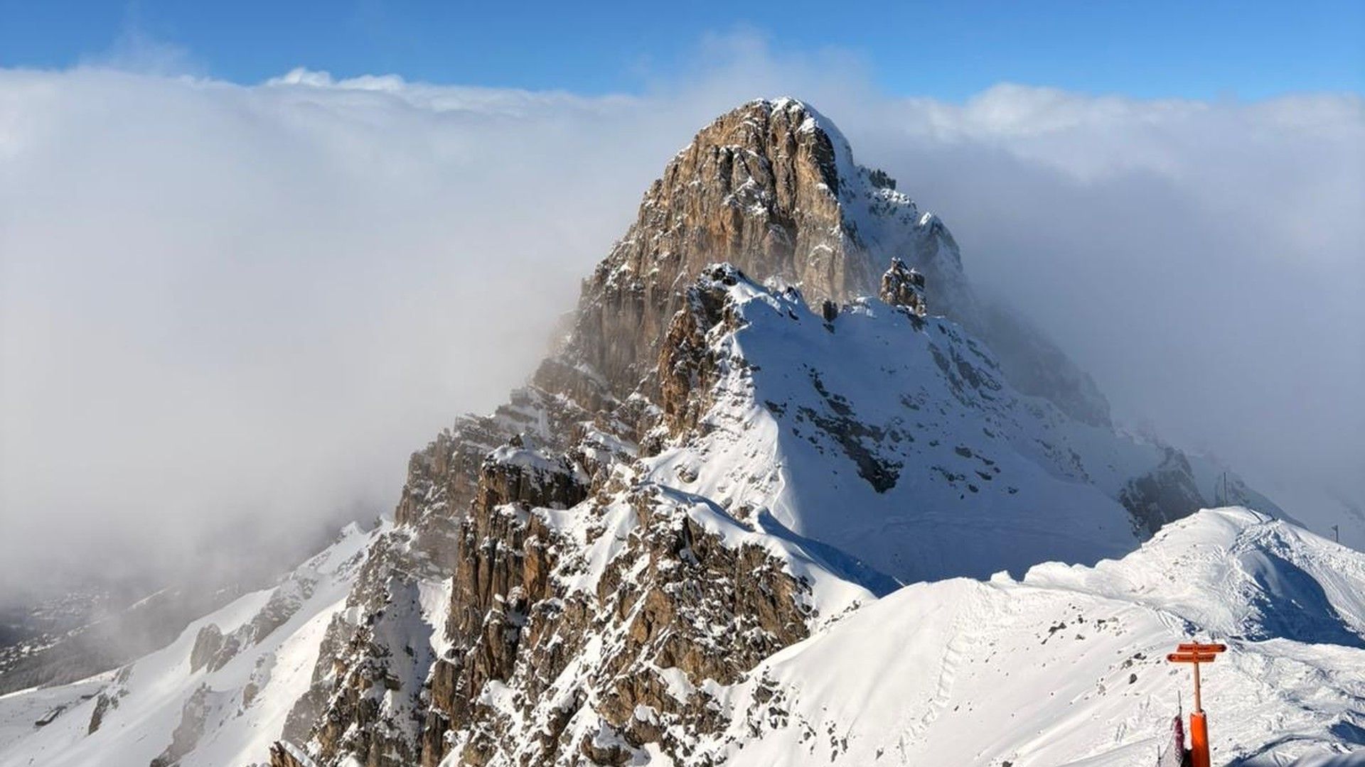 Snow-covered mountain peak above Courchevel ski slopes, with a lift pole in the foreground.