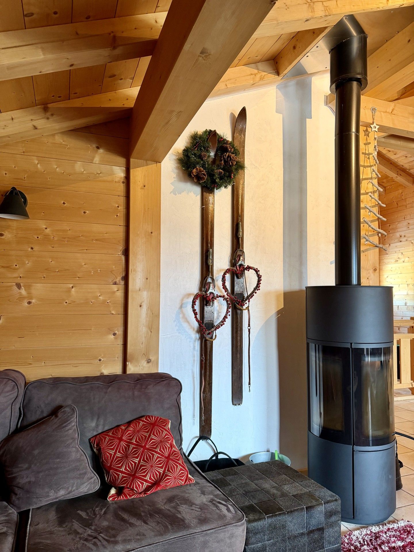 Wooden alpine cabin interior with a modern pellet stove, cushioned sofa, and hanging decorative heart ornaments