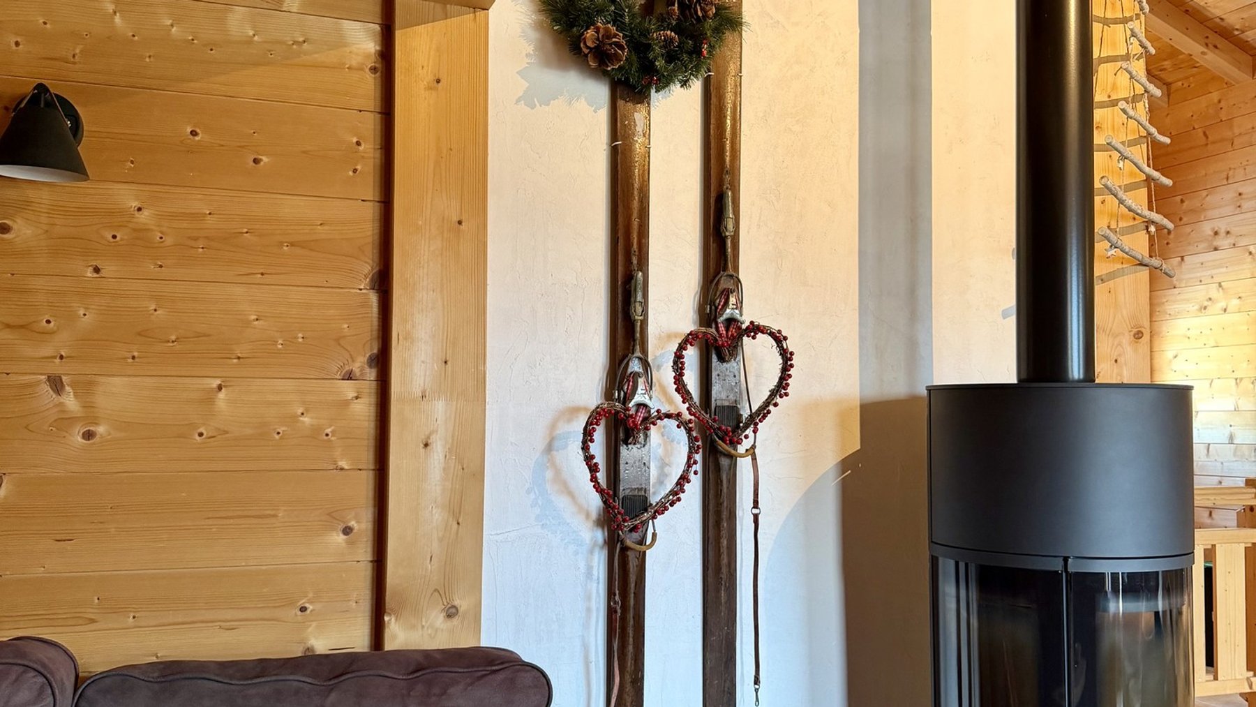 Wooden alpine cabin interior with a modern pellet stove, cushioned sofa, and hanging decorative heart ornaments