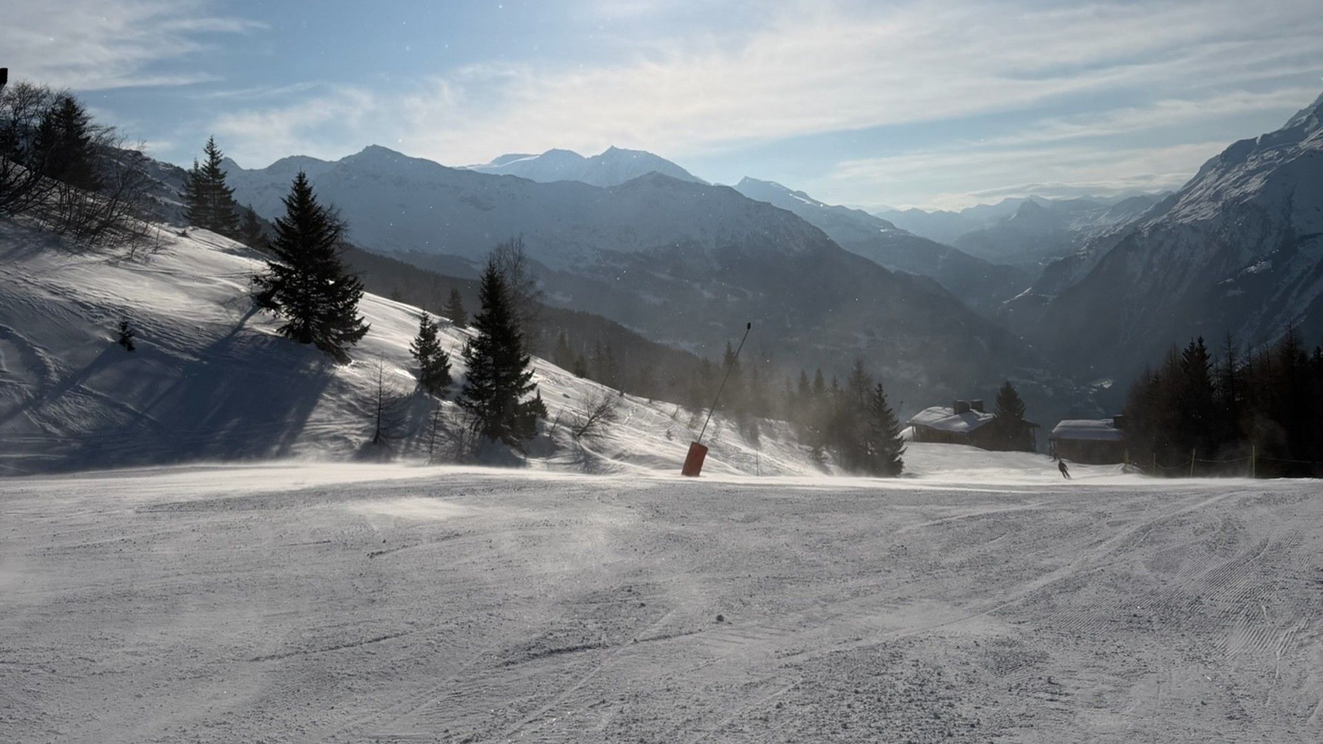 Snowy beginner piste in La Rosière, with pine trees, mountain peaks and the sunlit Tarentaise valley beyond