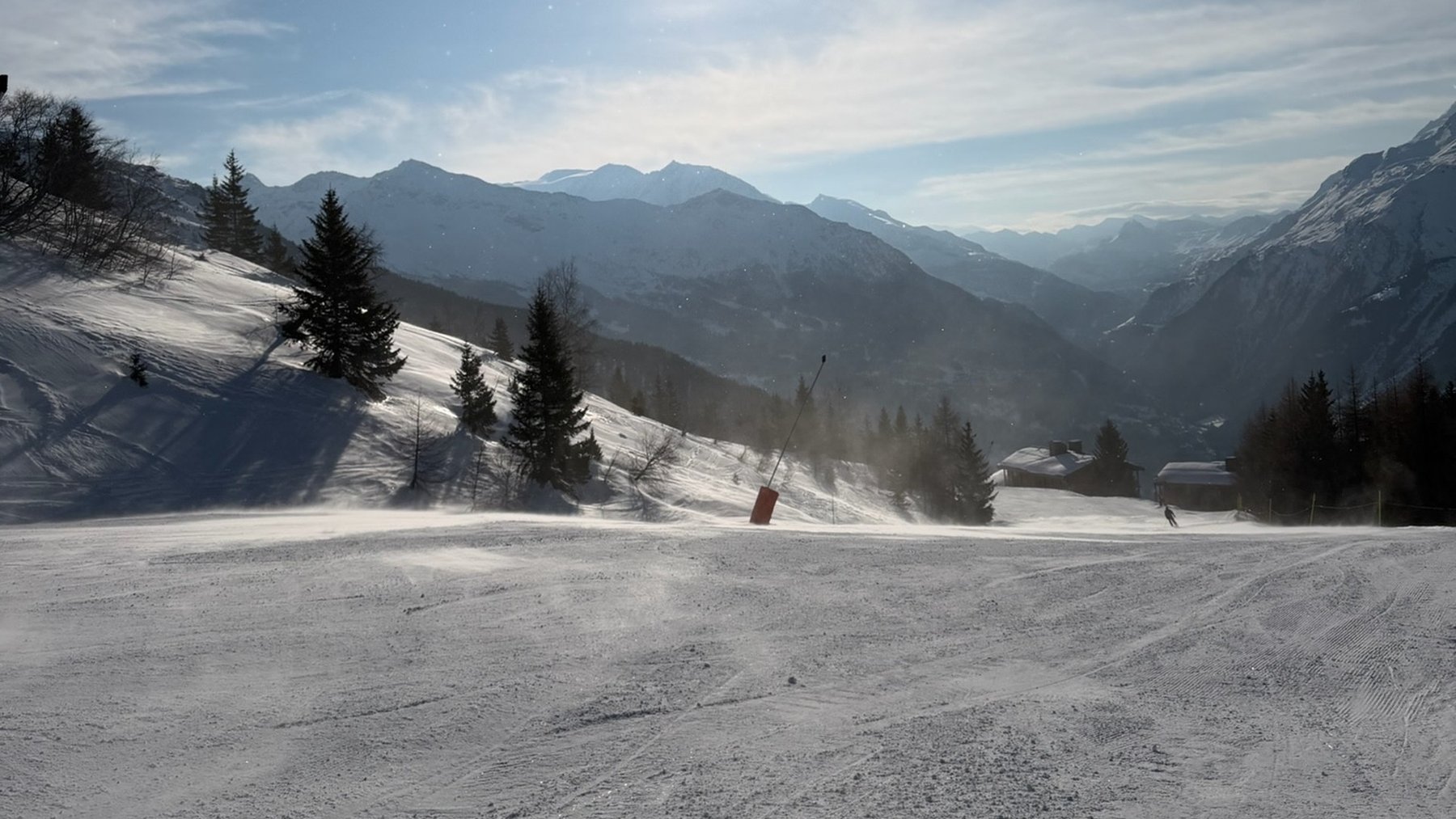 Snowy beginner piste in La Rosière, with pine trees, mountain peaks and the sunlit Tarentaise valley beyond