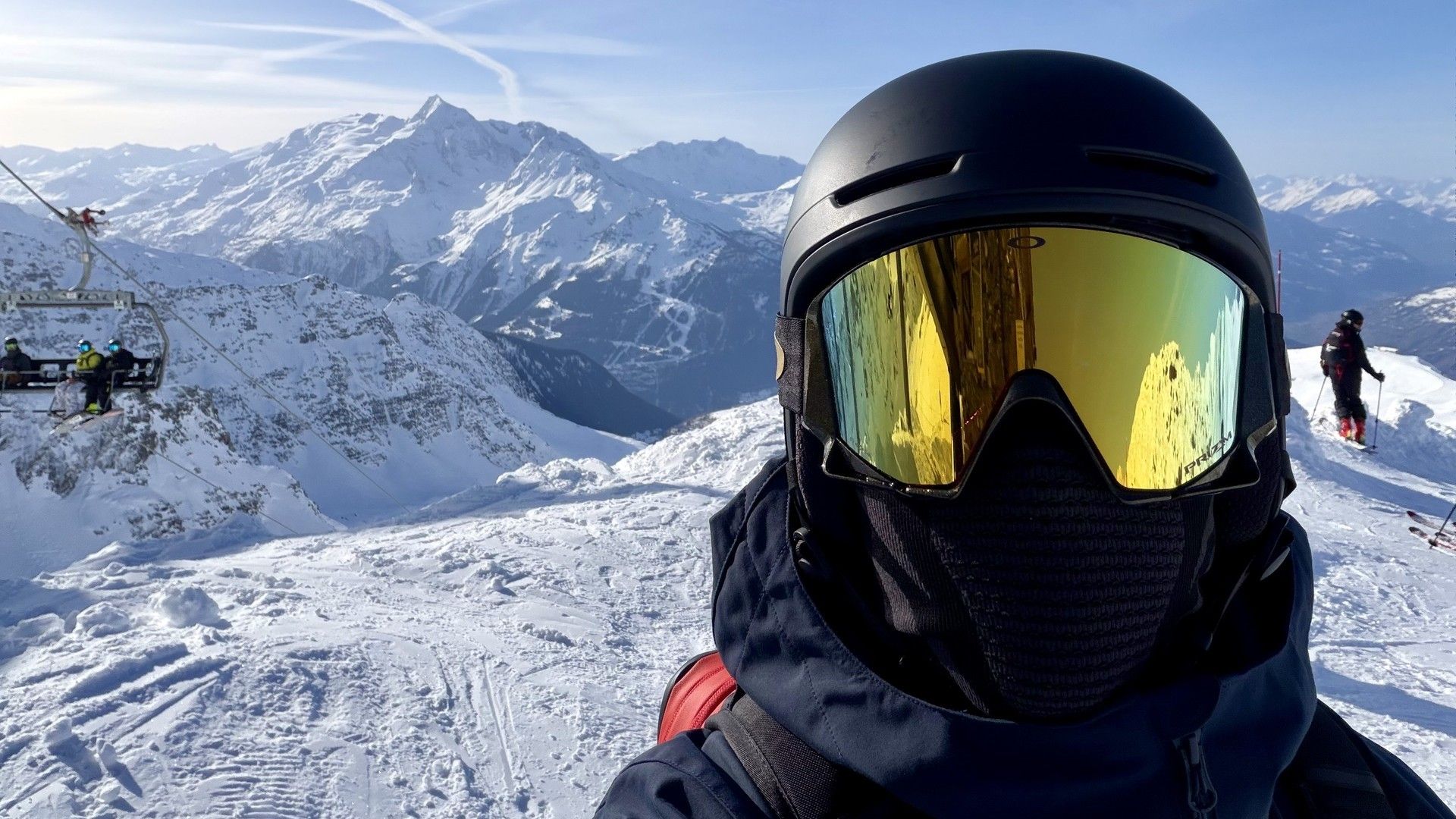 Ski rider in helmet and reflective goggles on a snowy mountain viewpoint under a clear sky.