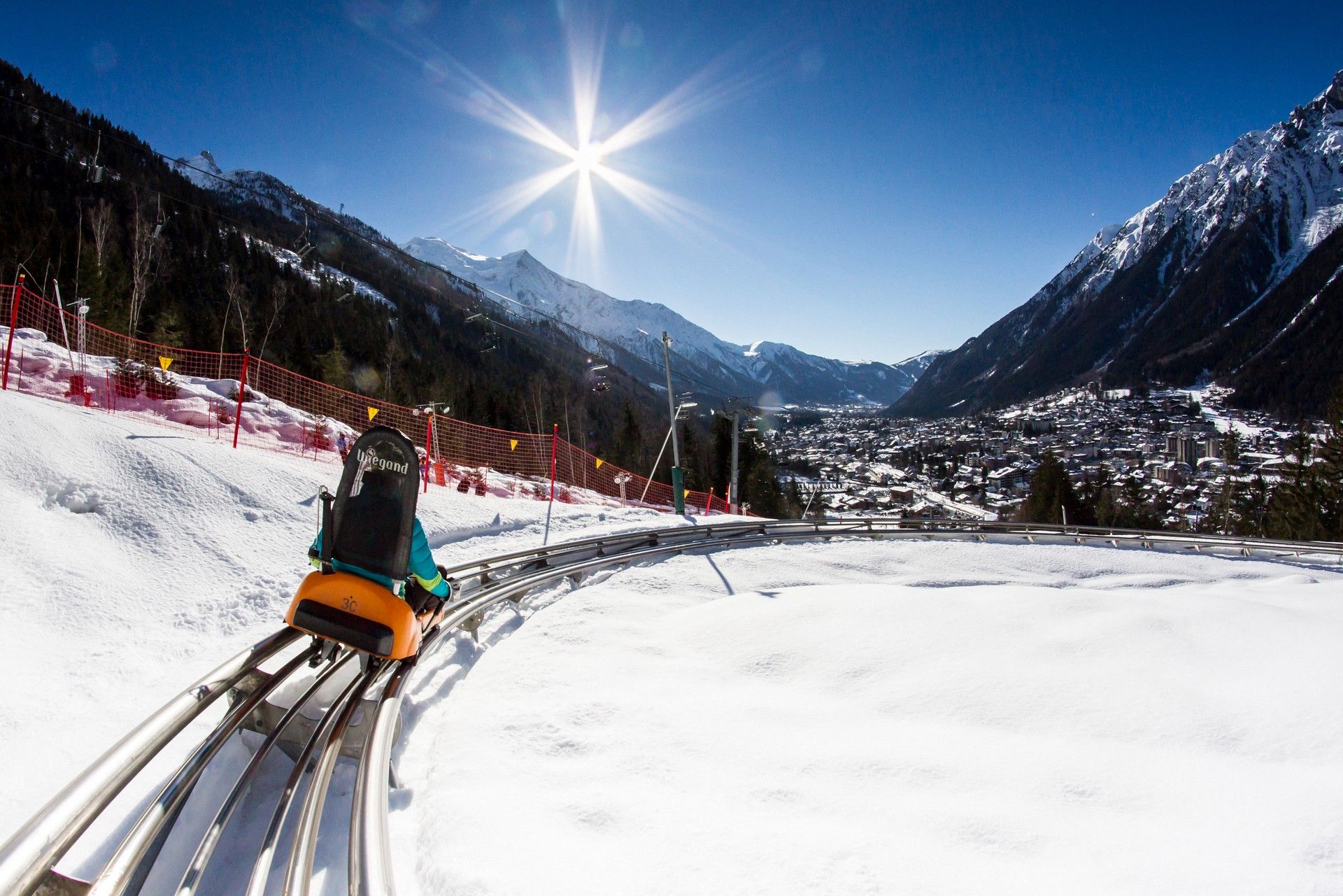 Forward view from a ski lift over groomed pistes, snowy valley and mountains under bright winter sun