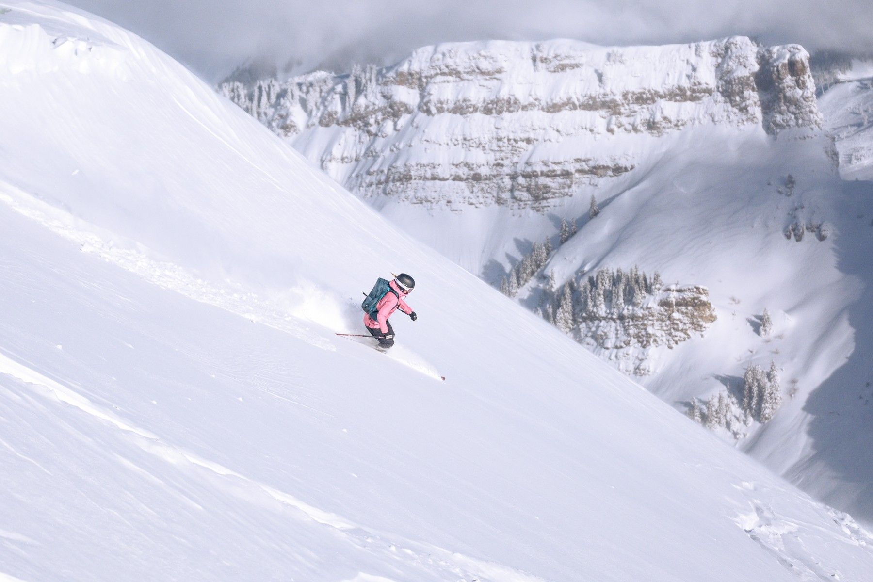 Skier carves through fresh powder on a steep alpine slope with mountains and skiers’ tracks behind