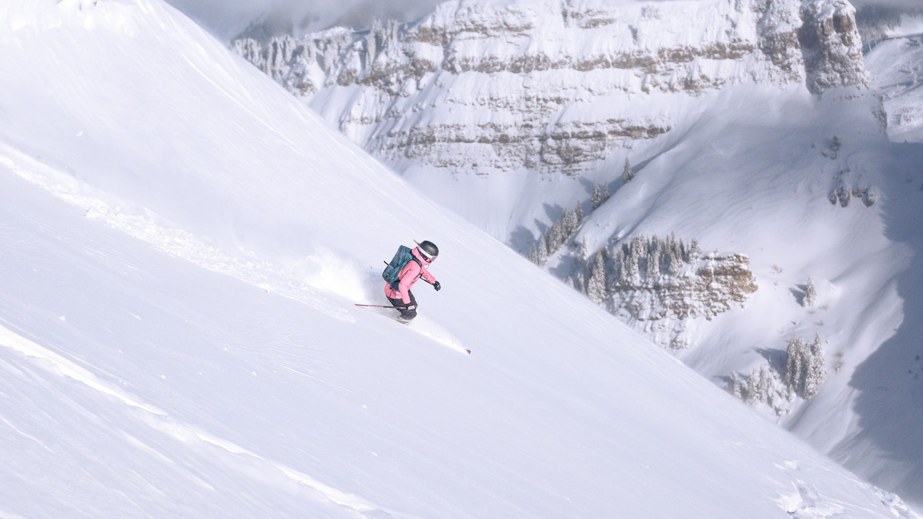 Skier carves through fresh powder on a steep alpine slope with mountains and skiers’ tracks behind
