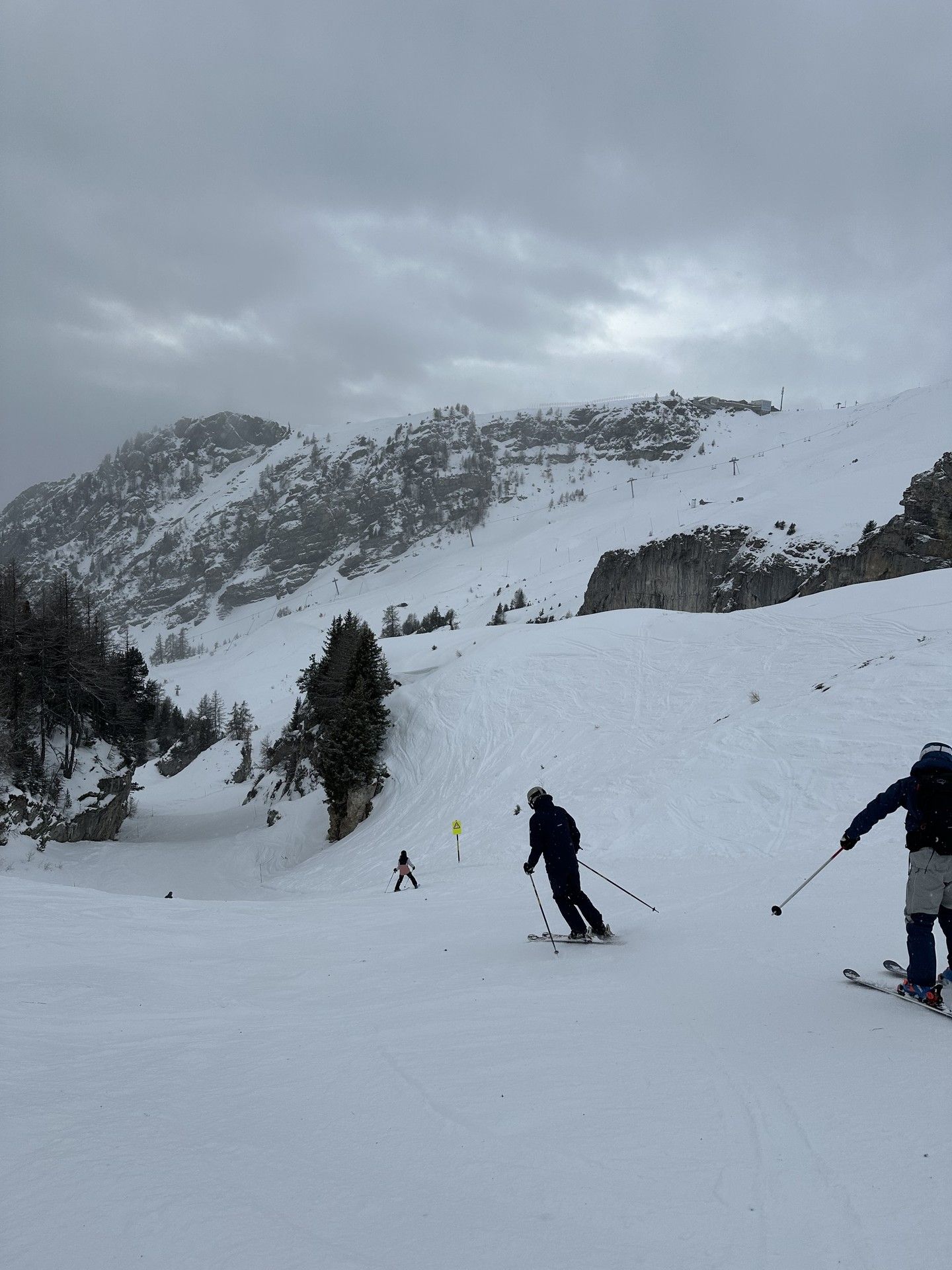 Skiers descending snowy alpine slopes under cloudy skies in a mountain ski resort